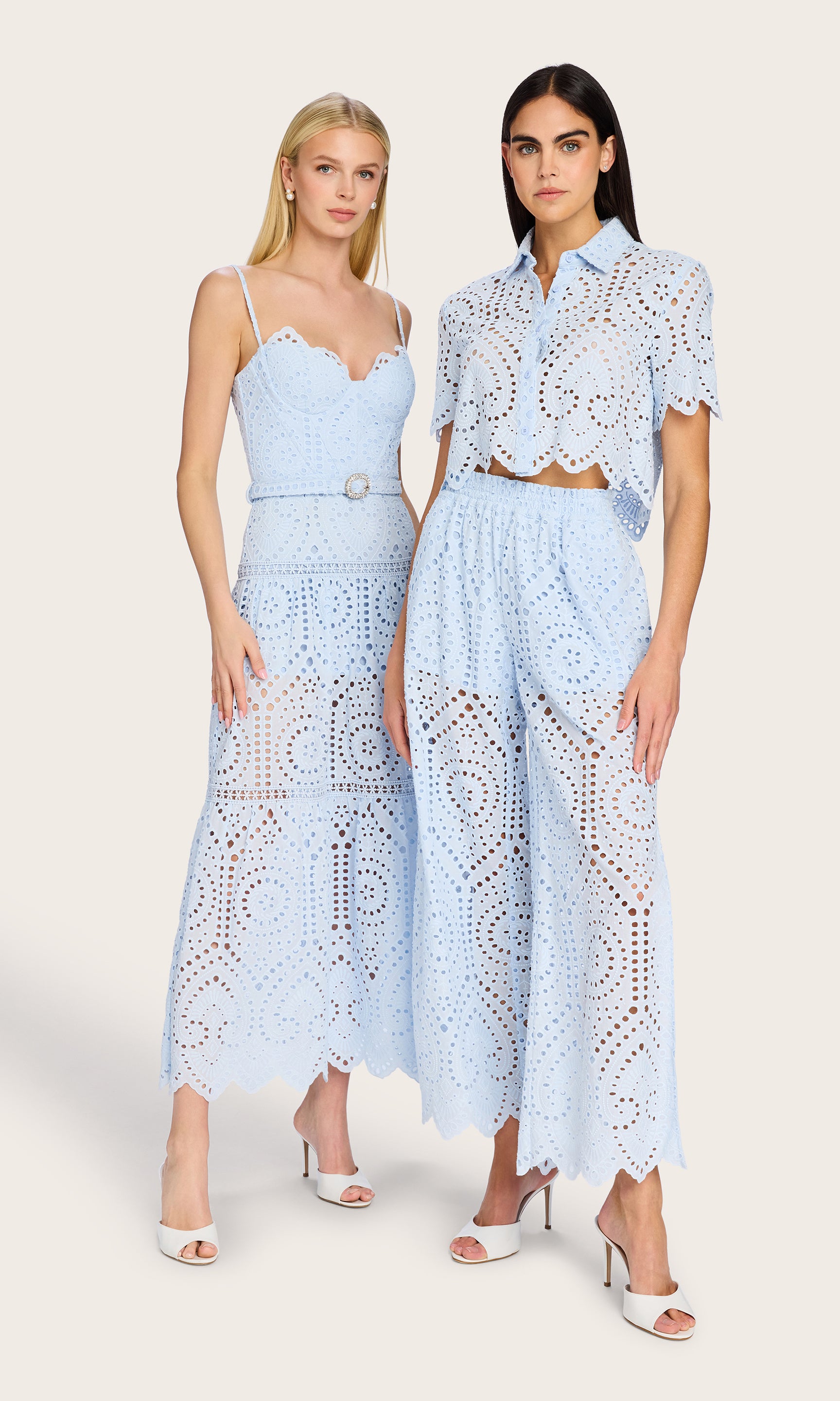 image of two models posing side by side both wearing eyelet lace styles, on the left she wears a blue opal dress and on the right she wears a matching top and pants blue opal eyelet lace set.