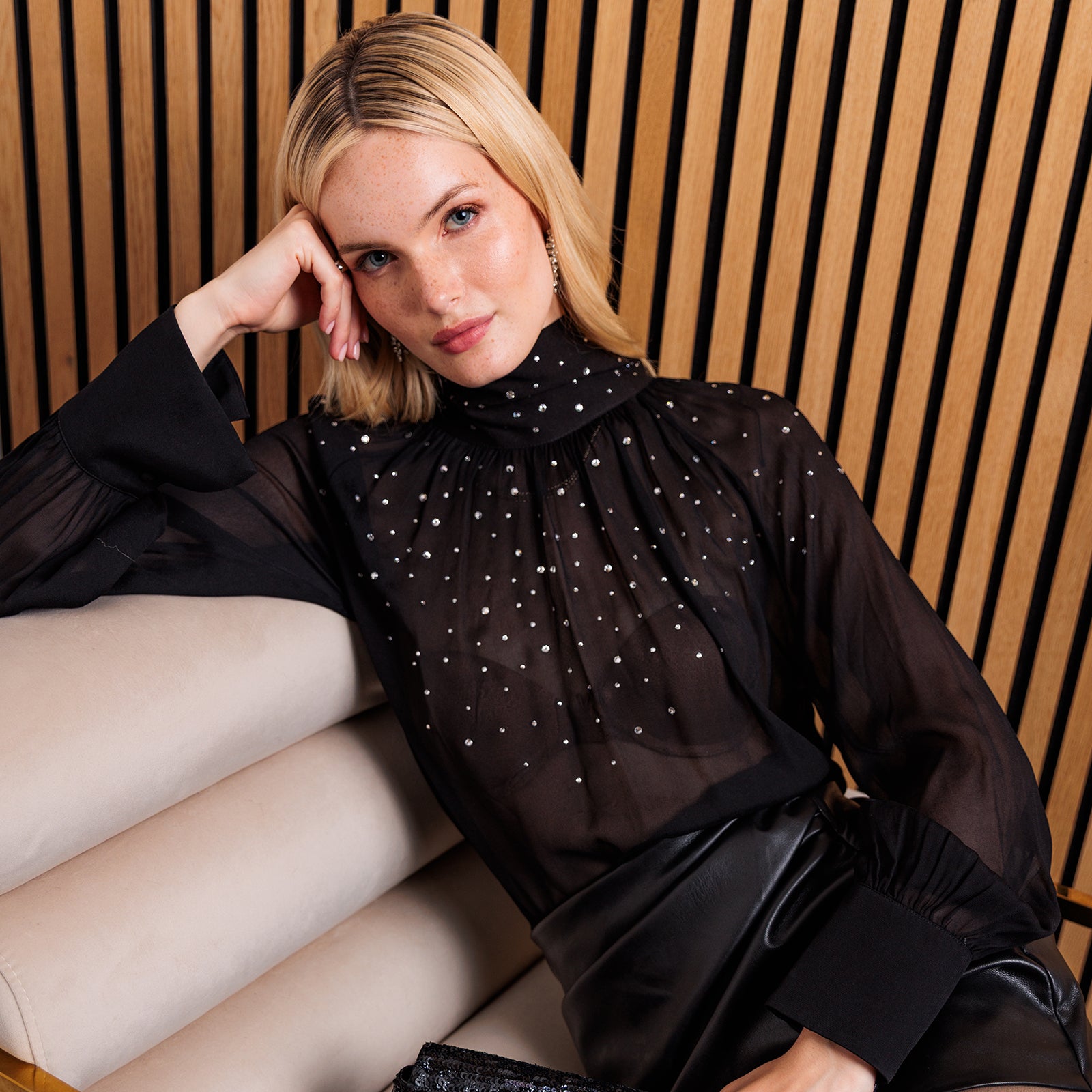 image of model sitting on a couch wearing a black blouse with crystal embellishments