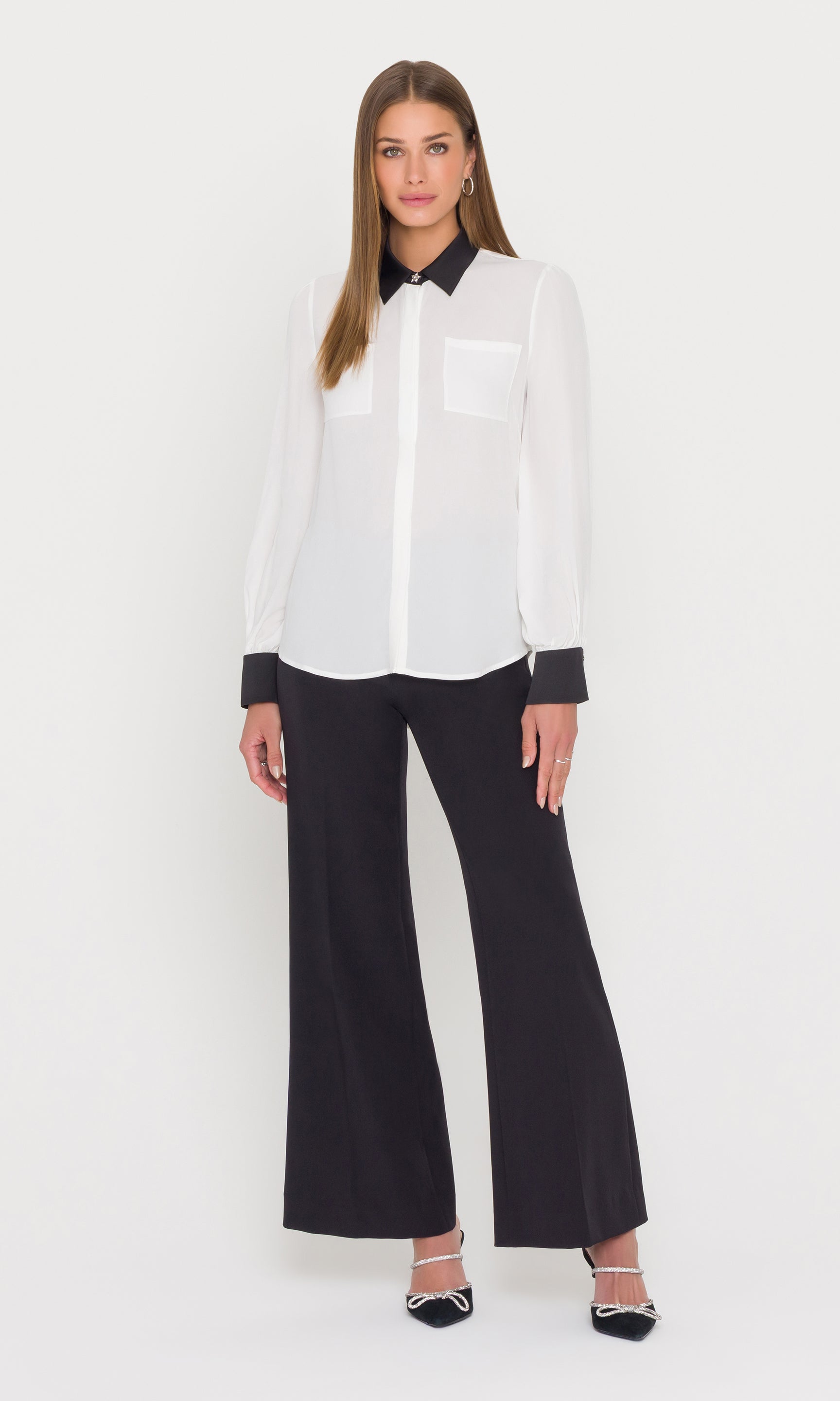 Woman wearing a white blouse with black collar and cuffs and black pants on a white background