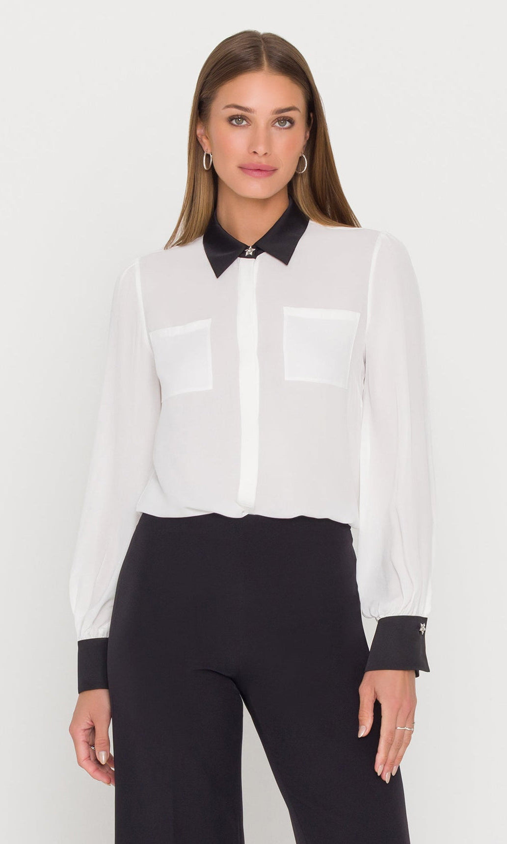 Woman wearing a white blouse with black collar and cuffs and black pants on a white background
