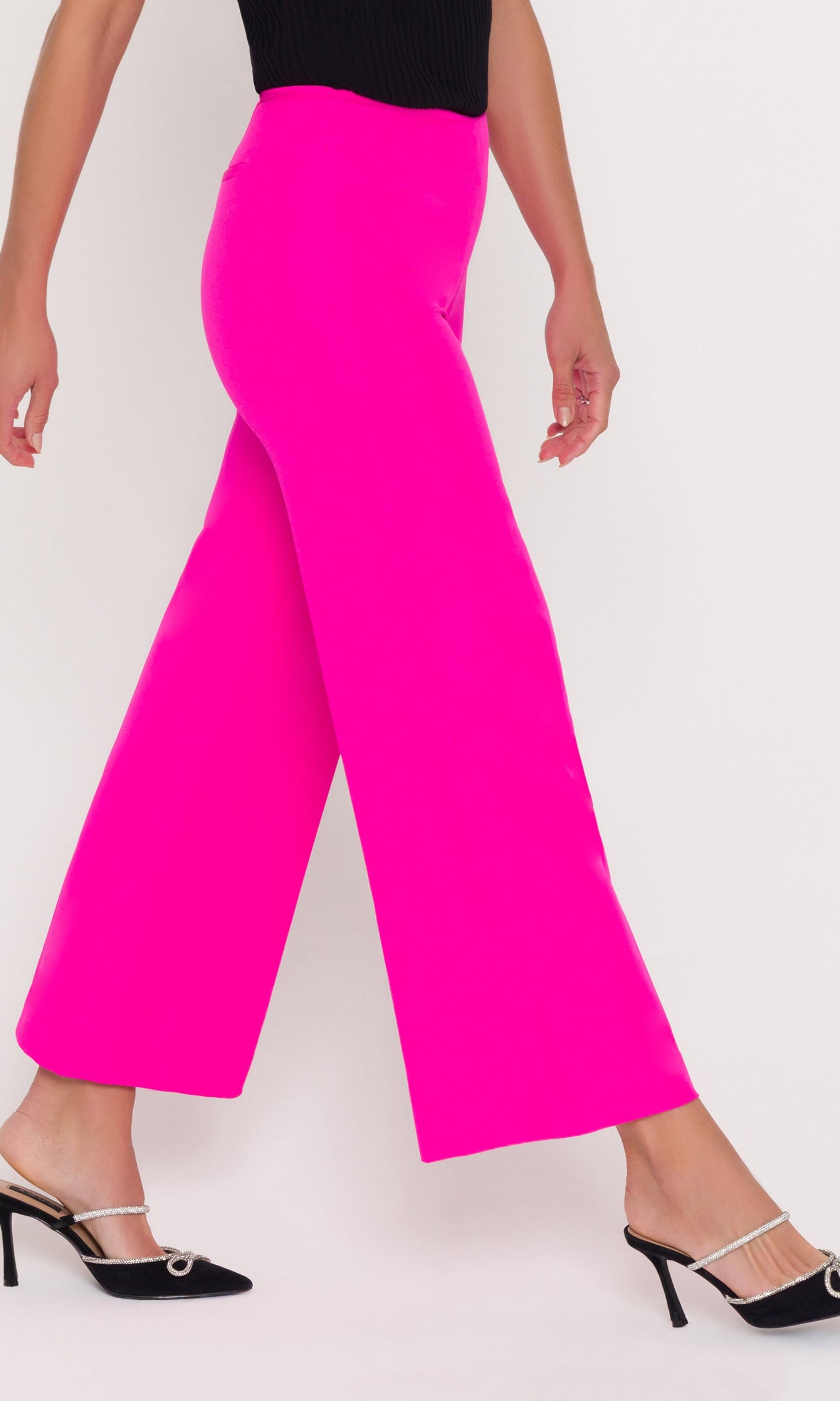 Person wearing a black top and bright pink pants on a white background