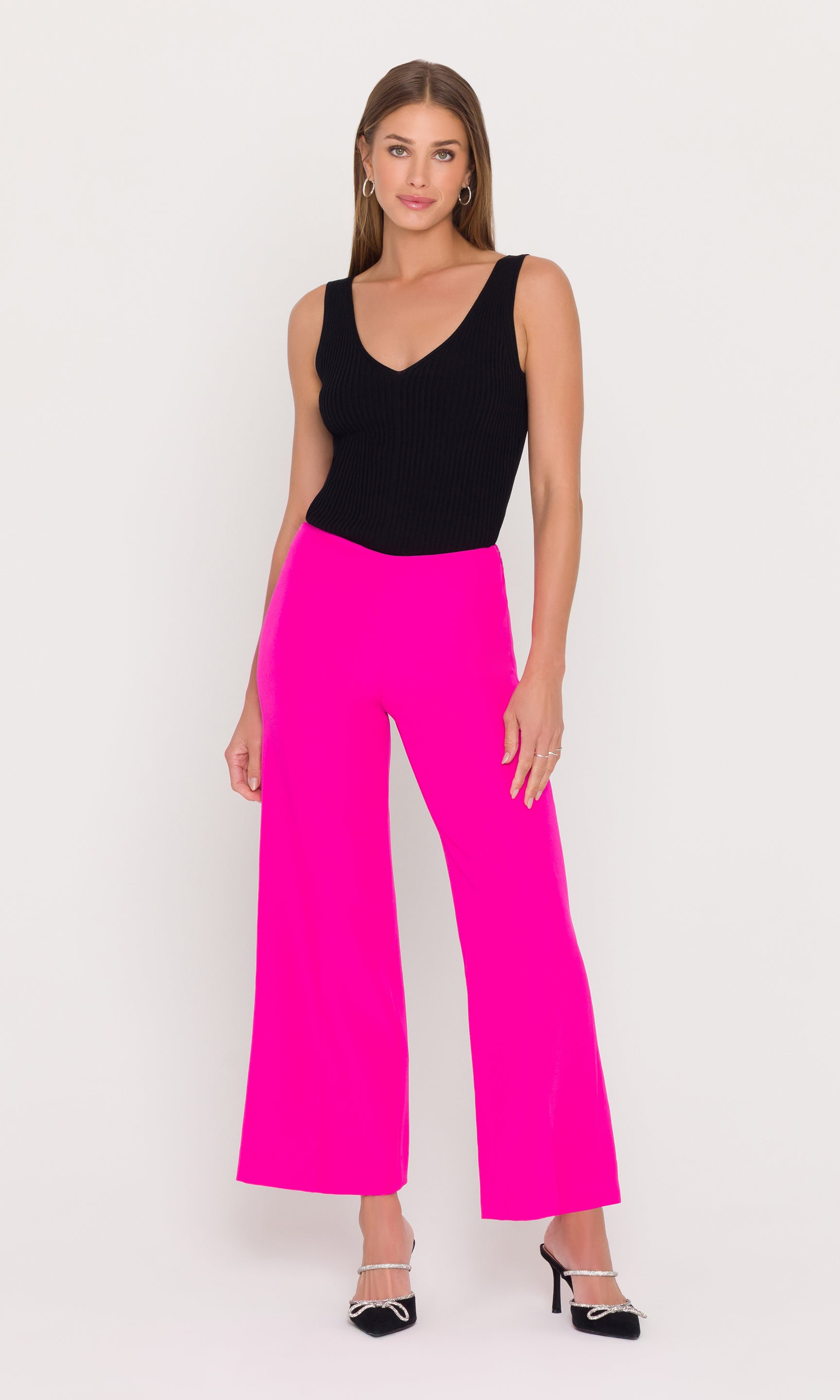 Woman wearing a black sleeveless top and magenta pants on a white background