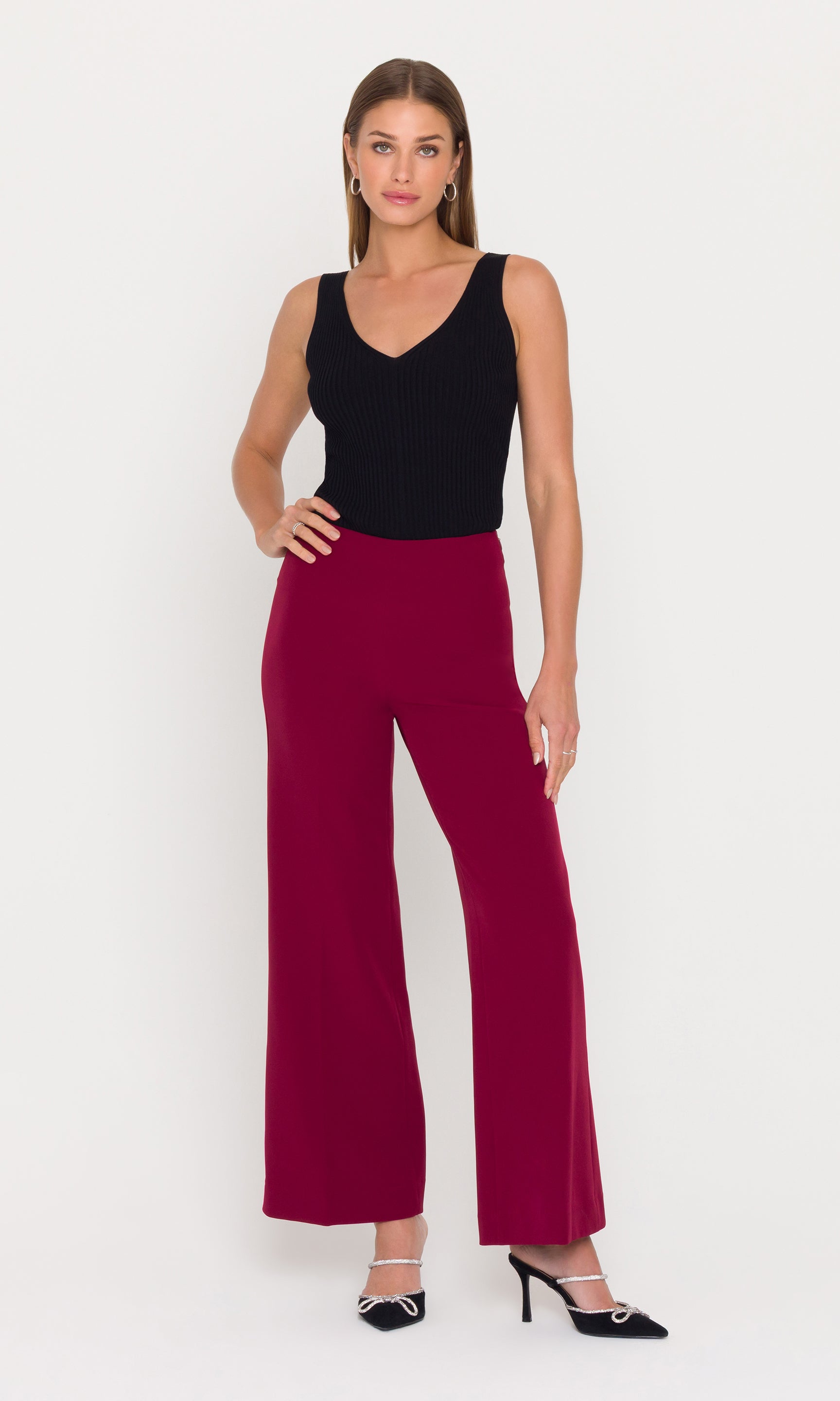 Model stands wearing a black sleeveless top and crimson wide leg pants.