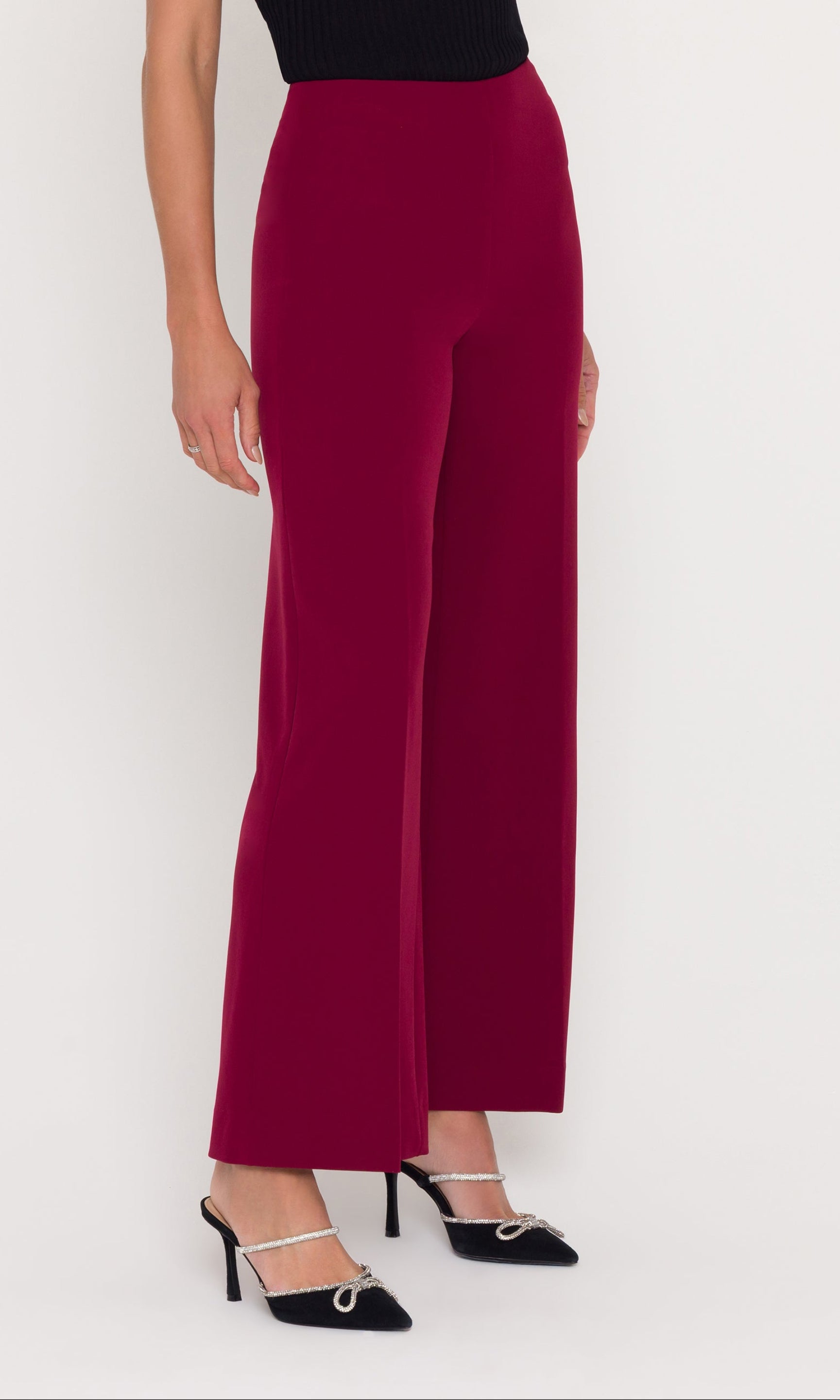 Side view of a person wearing crimson wide-leg pants with a black top on a white background