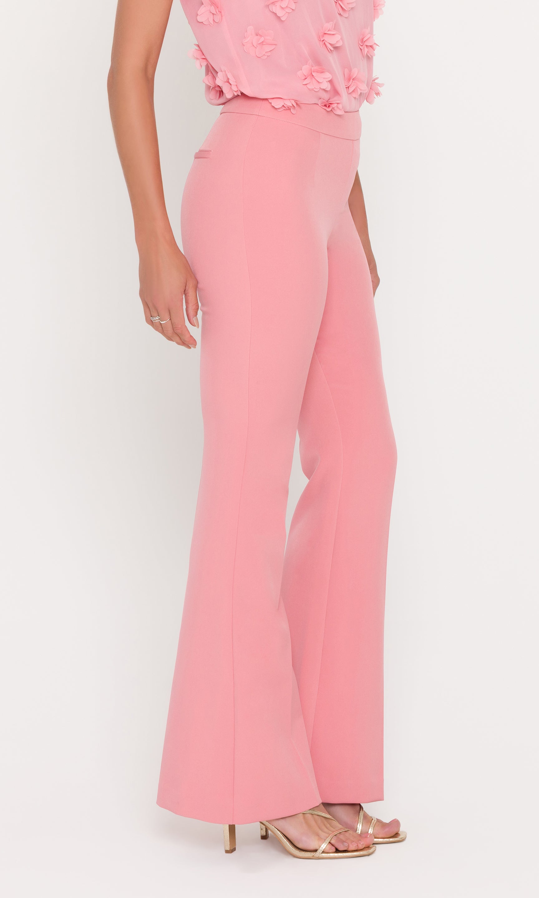 Person wearing a pink outfit with a floral top and flared pants on a white background