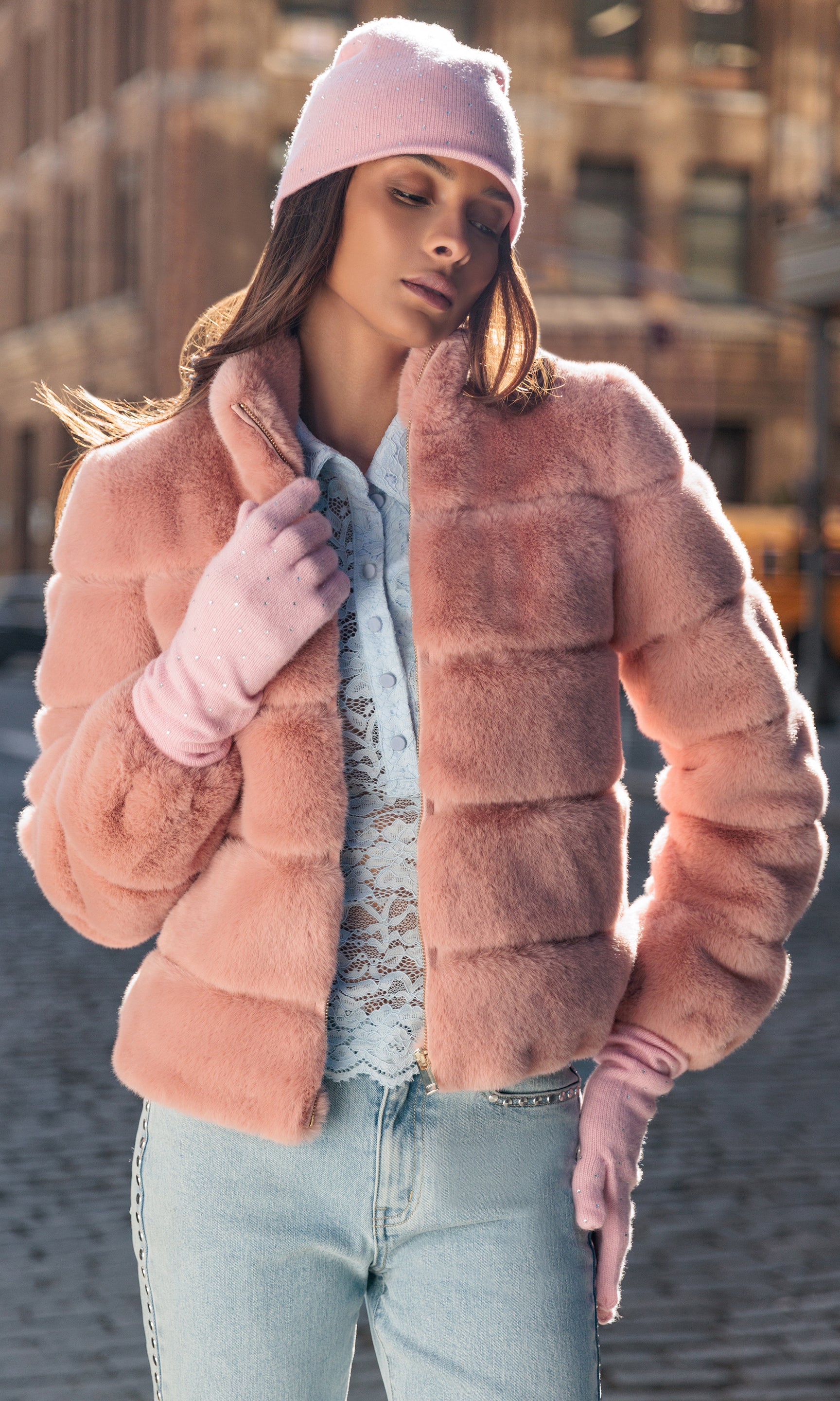 Woman wearing a pink fur coat, pink beanie, and light blue jeans outdoors.