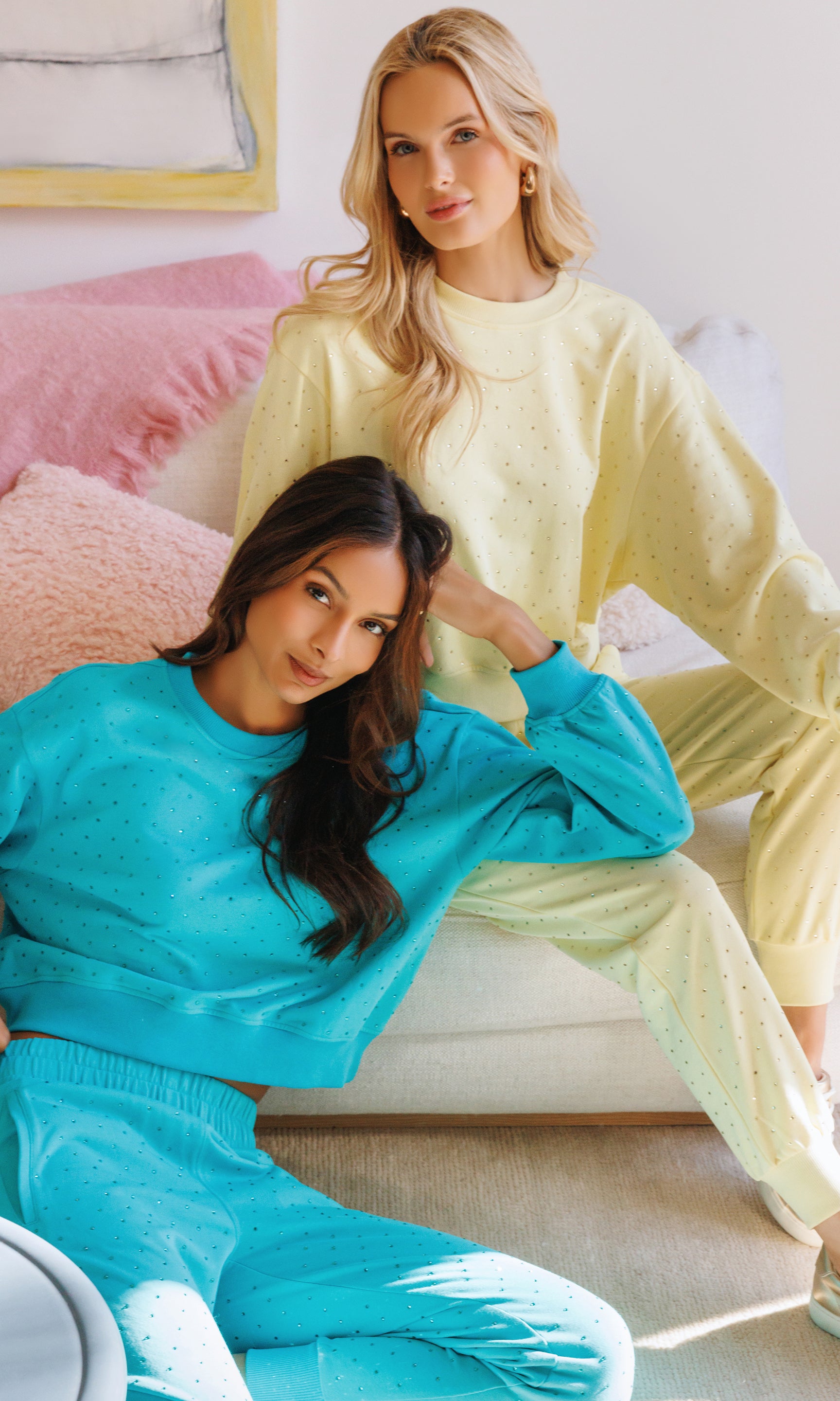 Two women in pastel sweatsuits sitting on a couch.