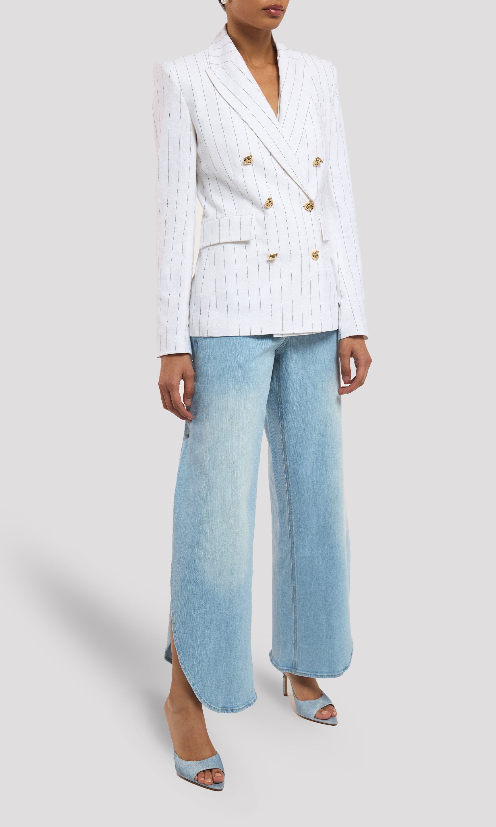 Person wearing a white blazer with gold buttons and light blue jeans on a white background