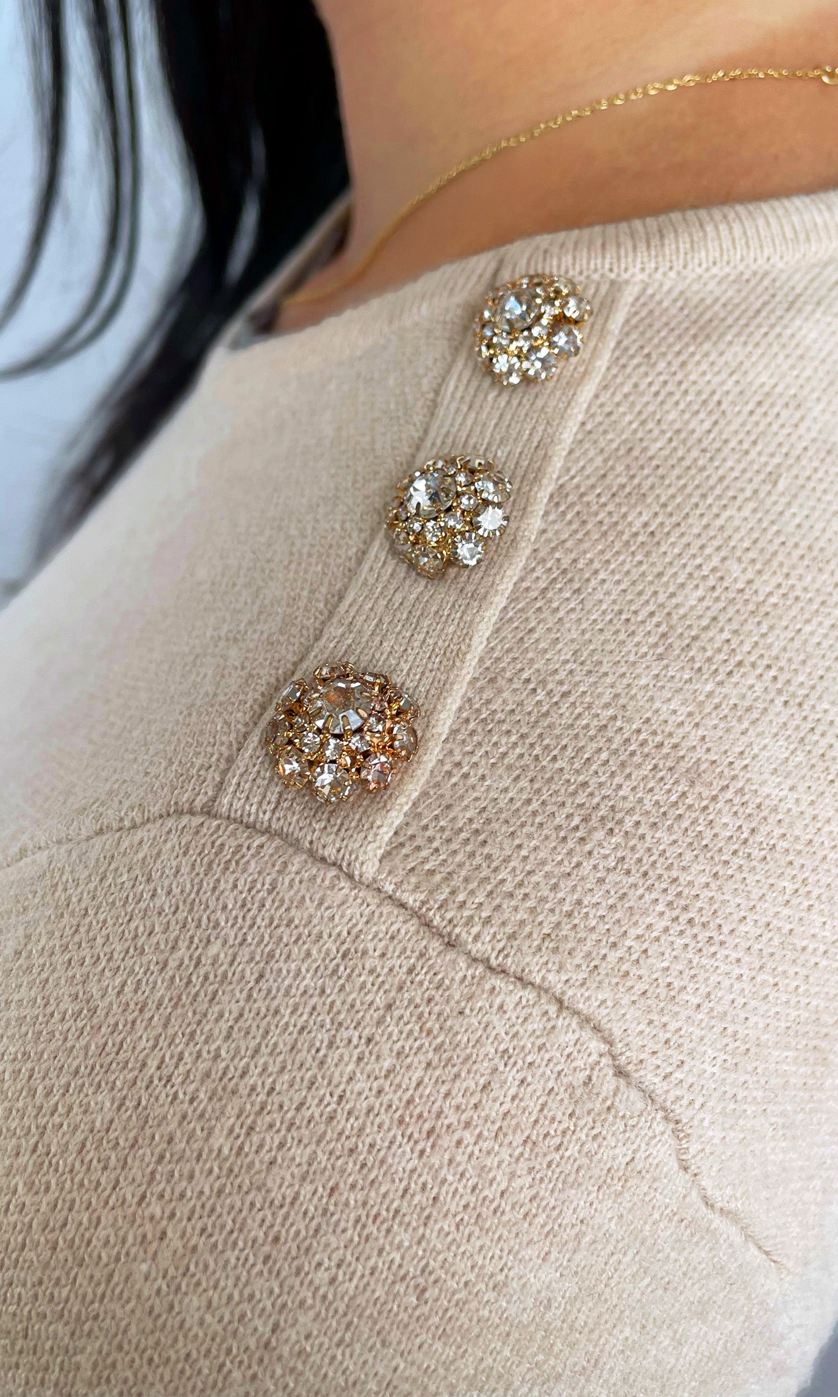 Close-up of a beige sweater with decorative buttons featuring gemstones.