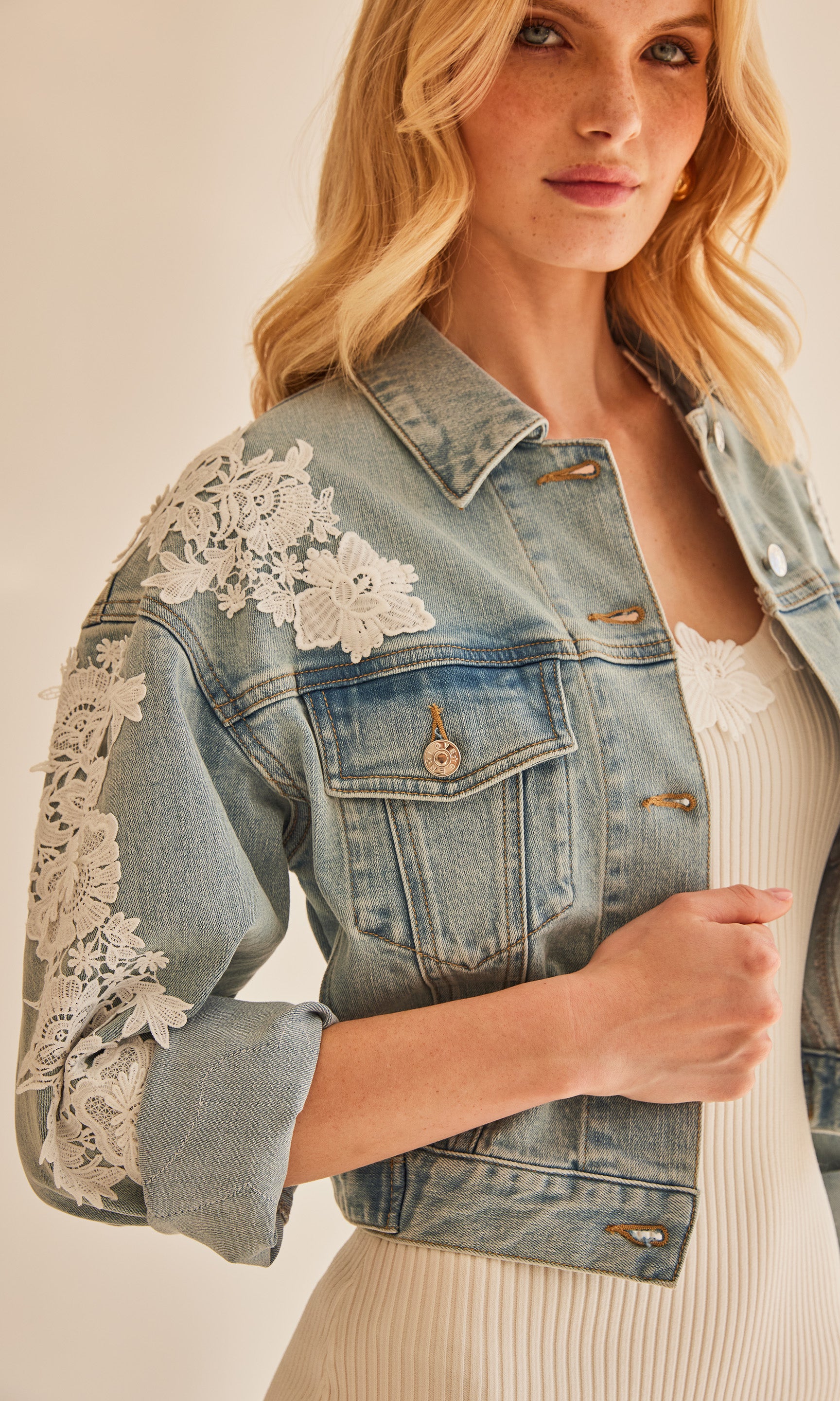 Close up of model wearing a denim jacket with white floral lace down the sleeves