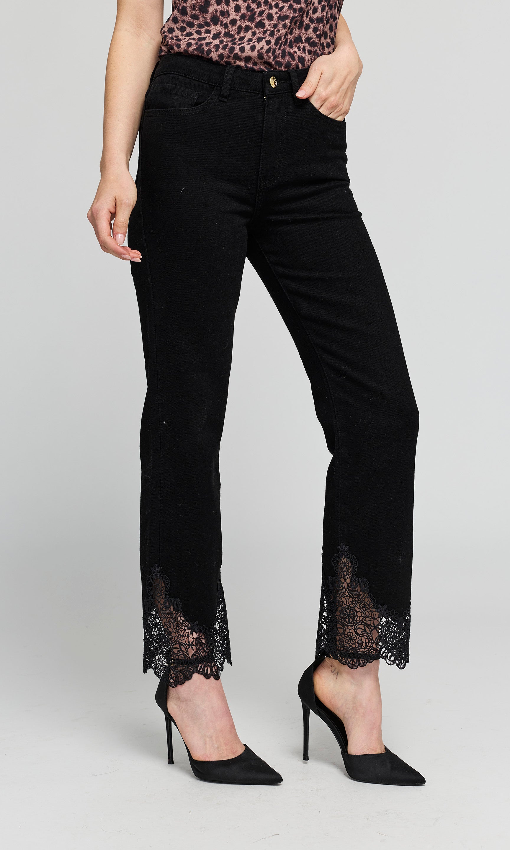 Side view of black cropped  jeans with black lace trim at the hem, shown on a model on a plain background.