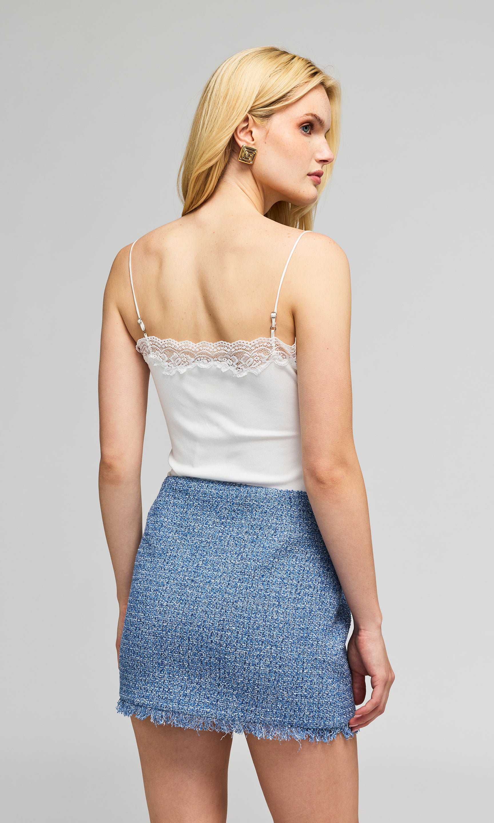 Back view of model in a white camisole top with lace trim and a blue tweed mini skirt against a plain background.