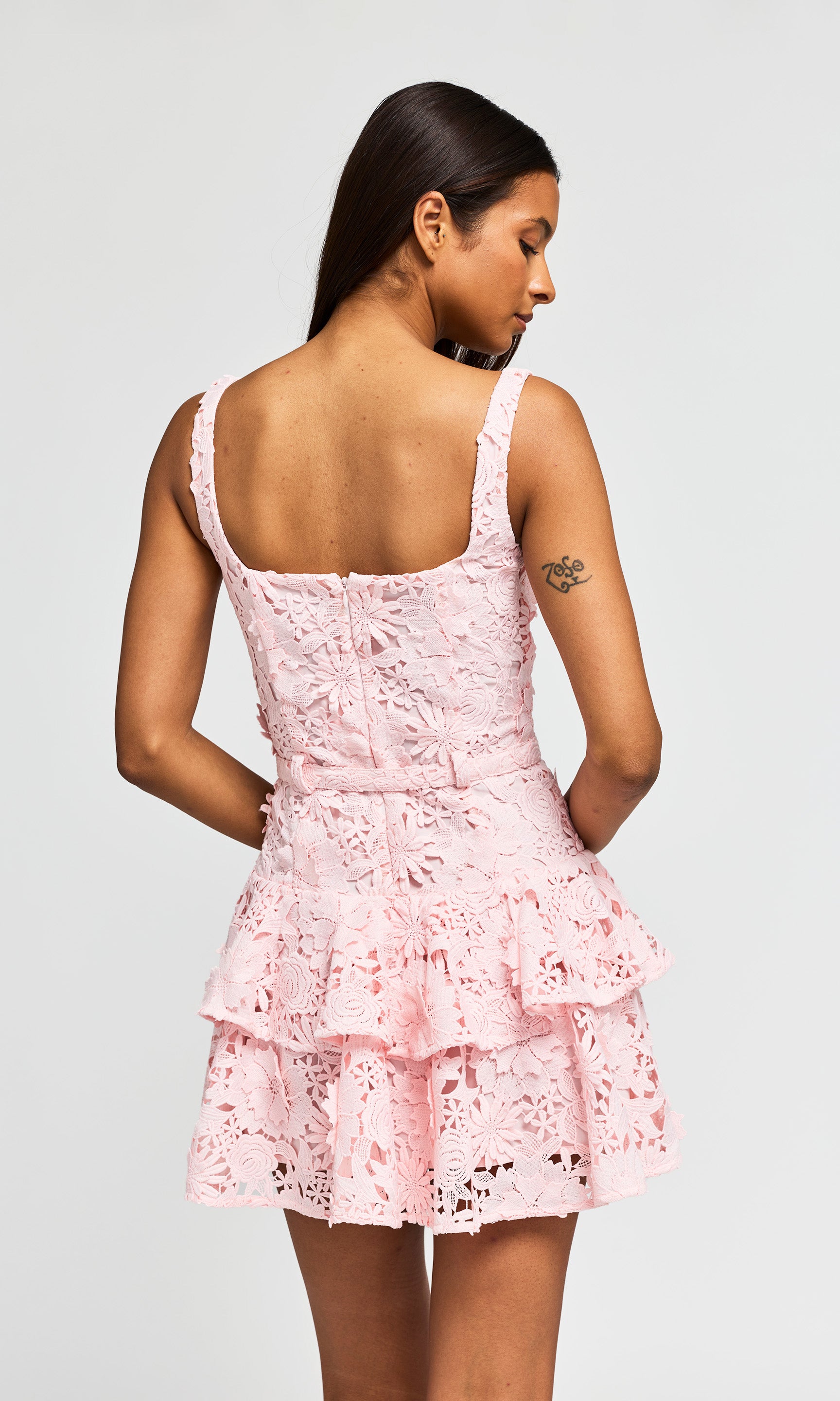 Back view of woman wearing a pink lace dress against a white background