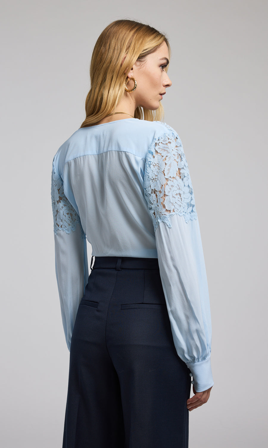 A model showcases a blue blouse featuring elegant lace sleeves, highlighting a stylish and sophisticated design.