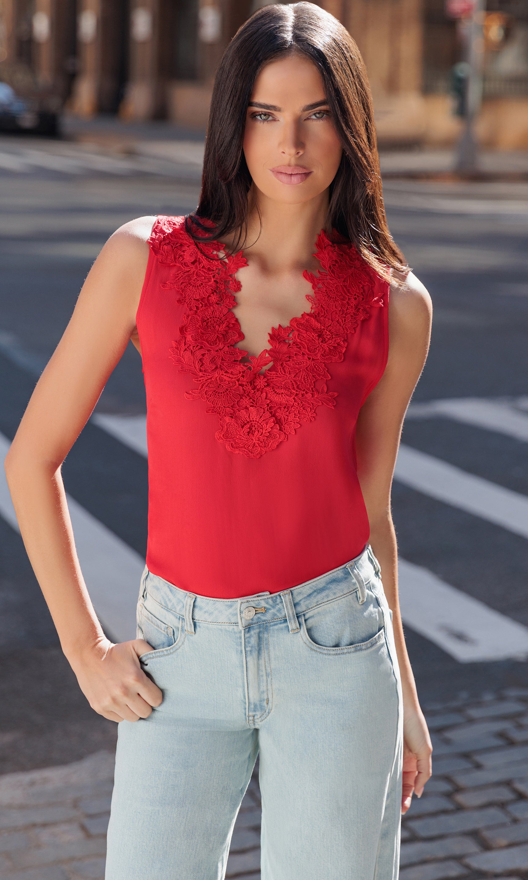 Woman wearing a red sleeveless top with floral details and light blue jeans on a street.