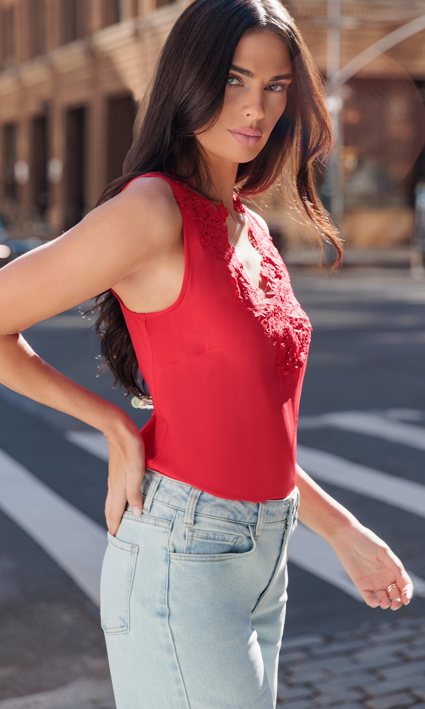 Woman wearing a red sleeveless top with floral details and light blue jeans on a street.