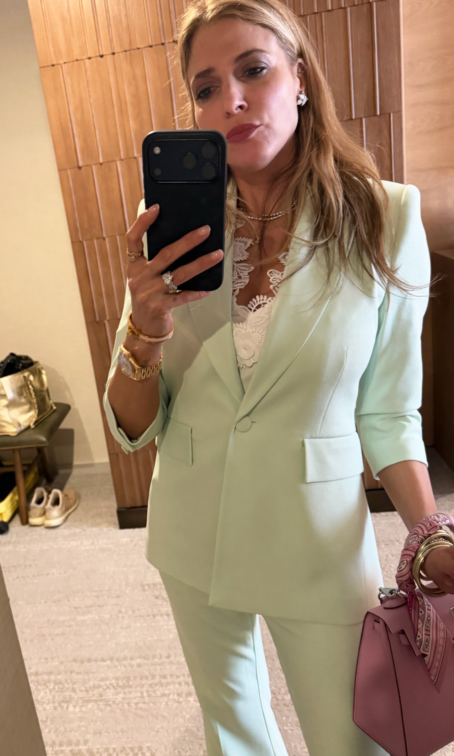 Founder Roni taking a mirror selfie wearing a light green suit and holding a pink handbag.
