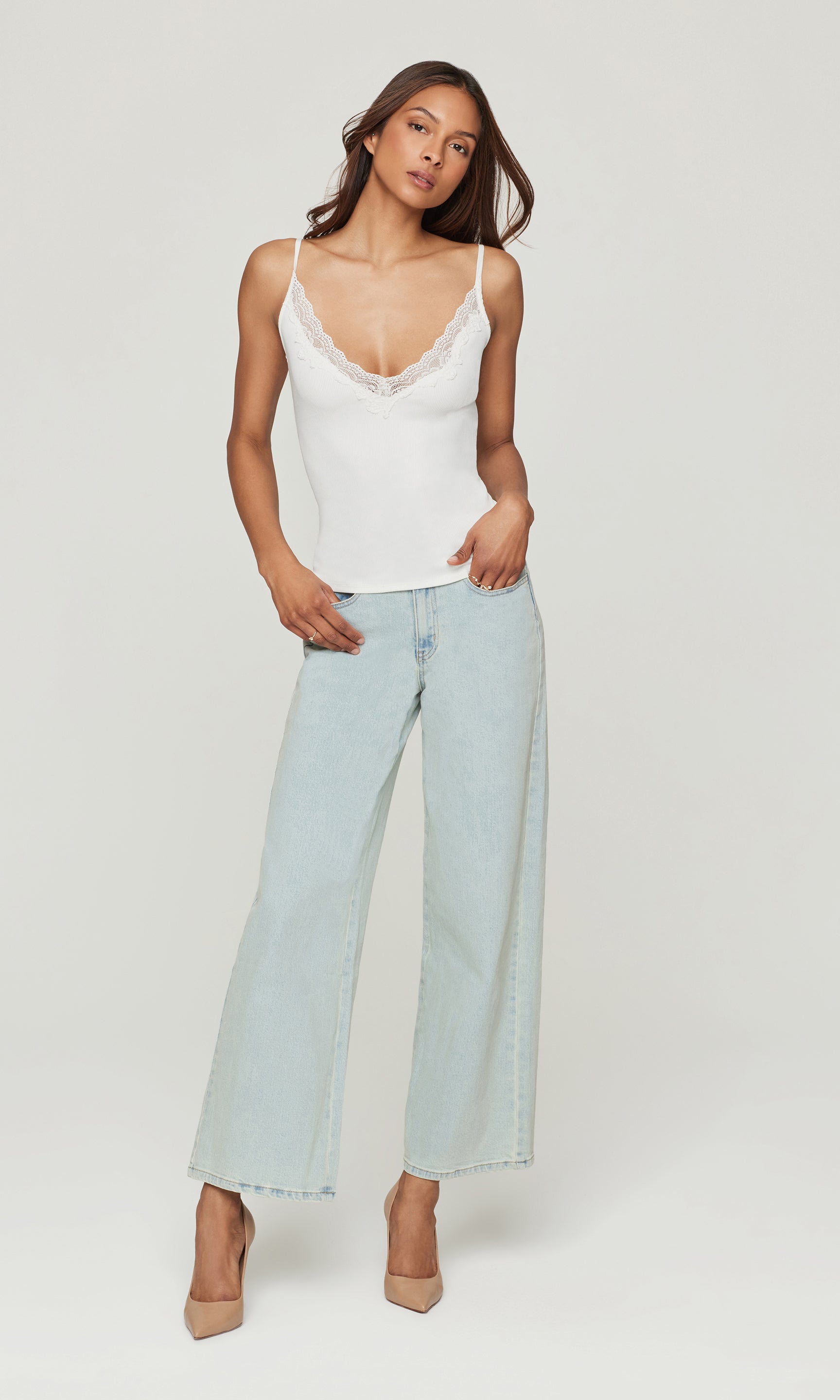 Full body image of model wearing a white cami with light blue jeans on a white background