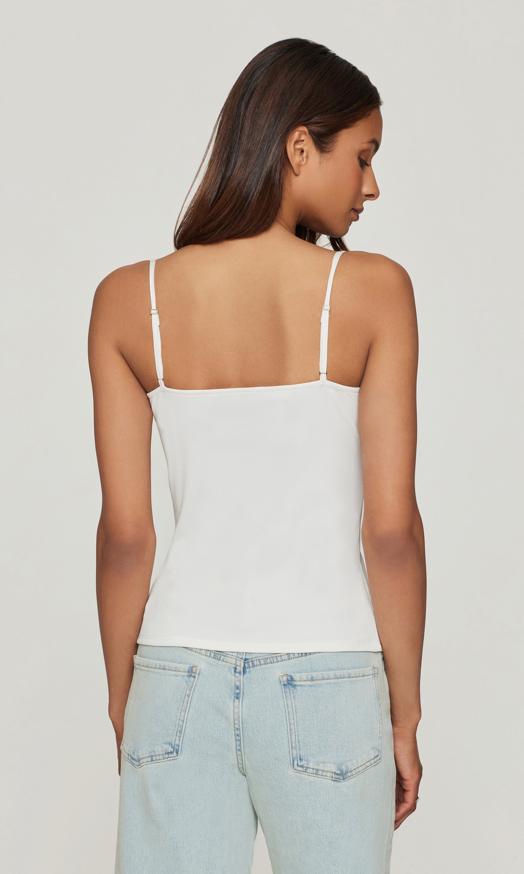 Back view image of model wearing a white cami with light blue jeans on a white background