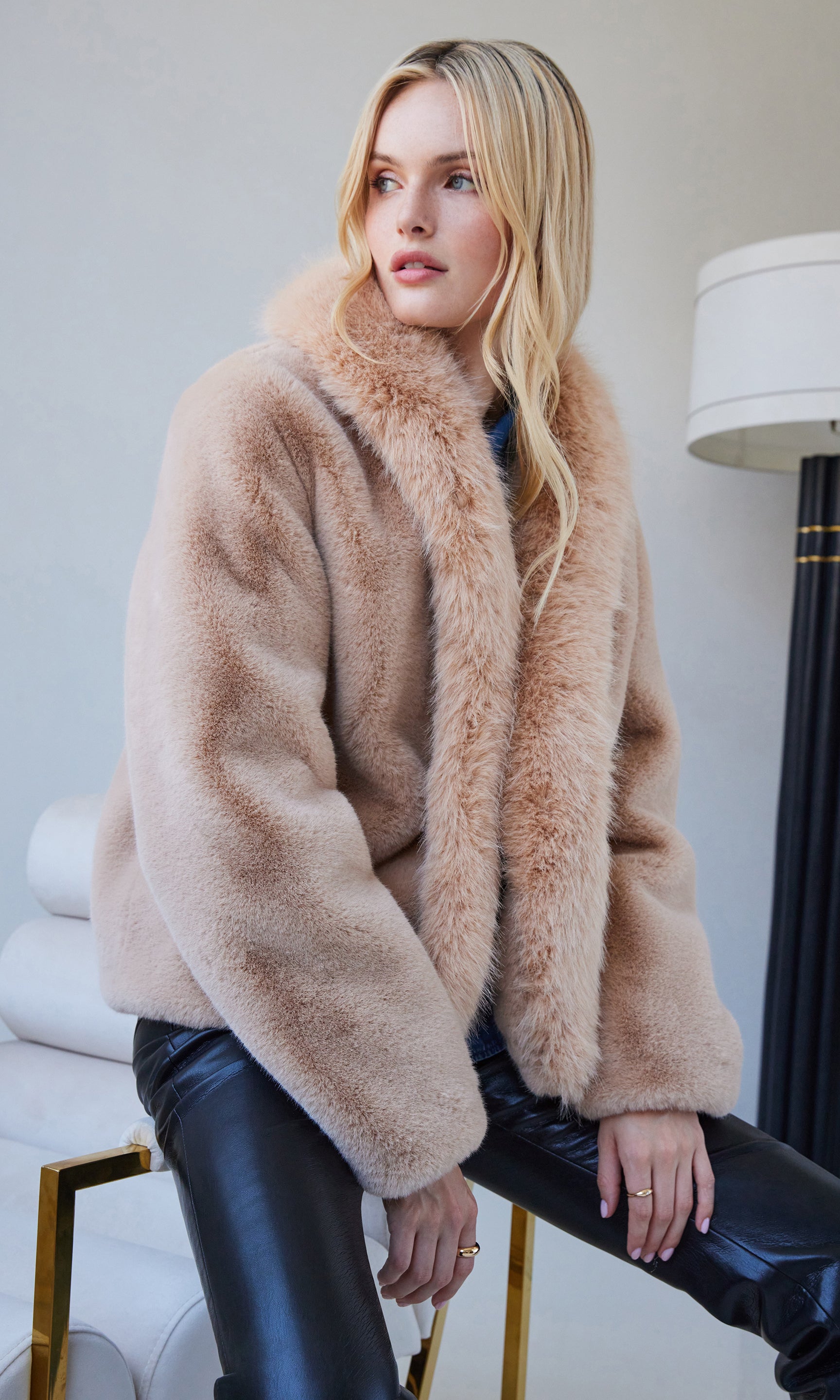 Standing pose with hands in pockets, showing the casual yet elegant appeal of the beige faux fur jacket with black leather pants.