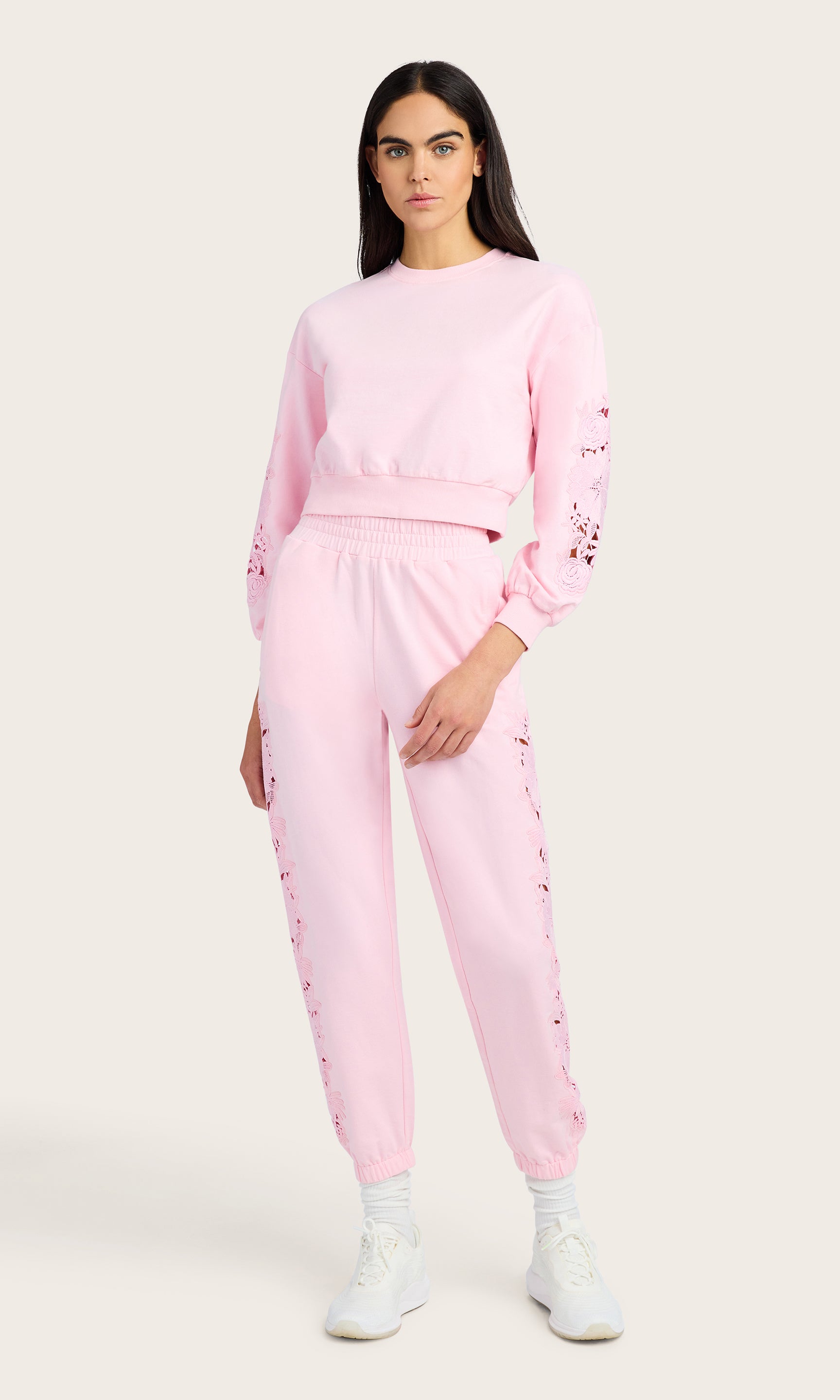 full body image of model wearing the Arabella pink sweatshirt with lace detail on the sleeves, paired with matching pink joggers and white sneakers