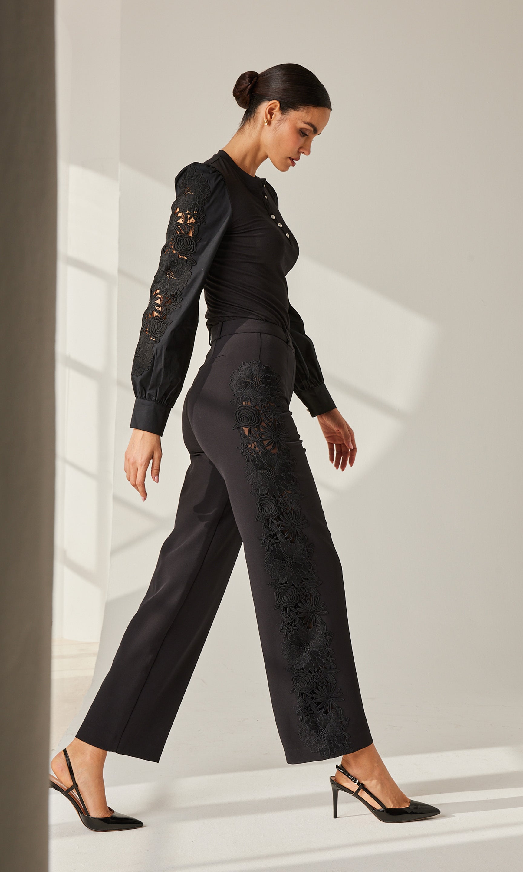 Woman walking in heels while wearing a black lace combo blouse and matching  black lace combo pants.