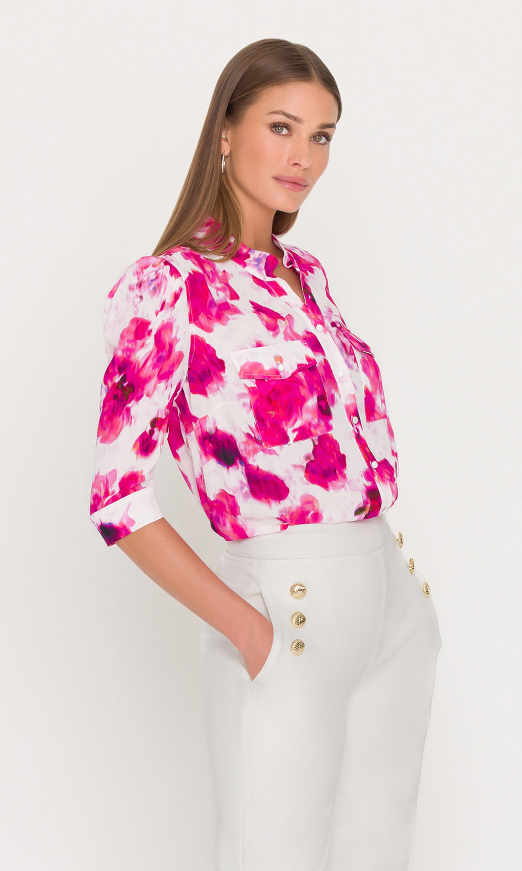Side view of woman wearing a colorful floral blouse and white pants on a white background