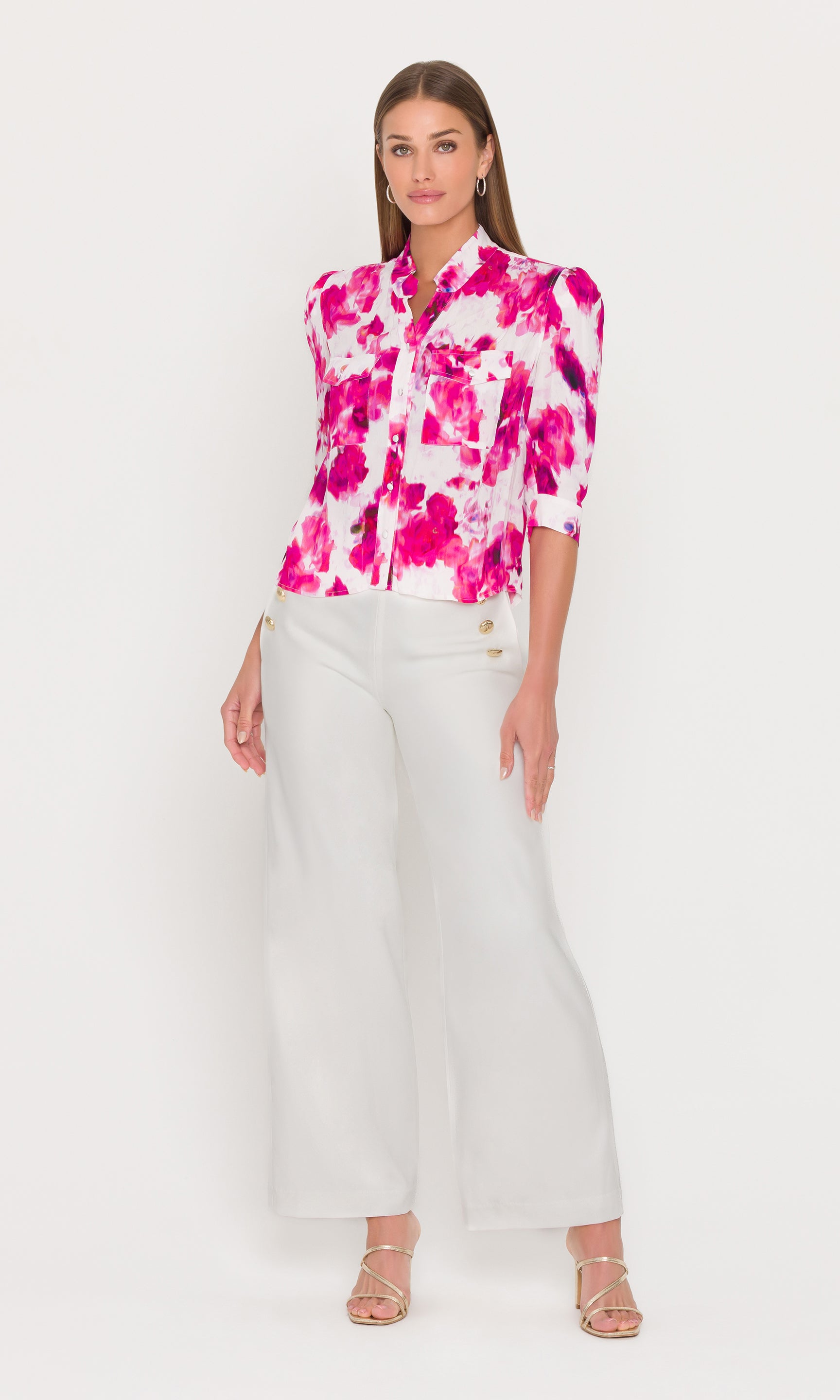 Woman wearing a pink floral blouse and white pants on a white background
