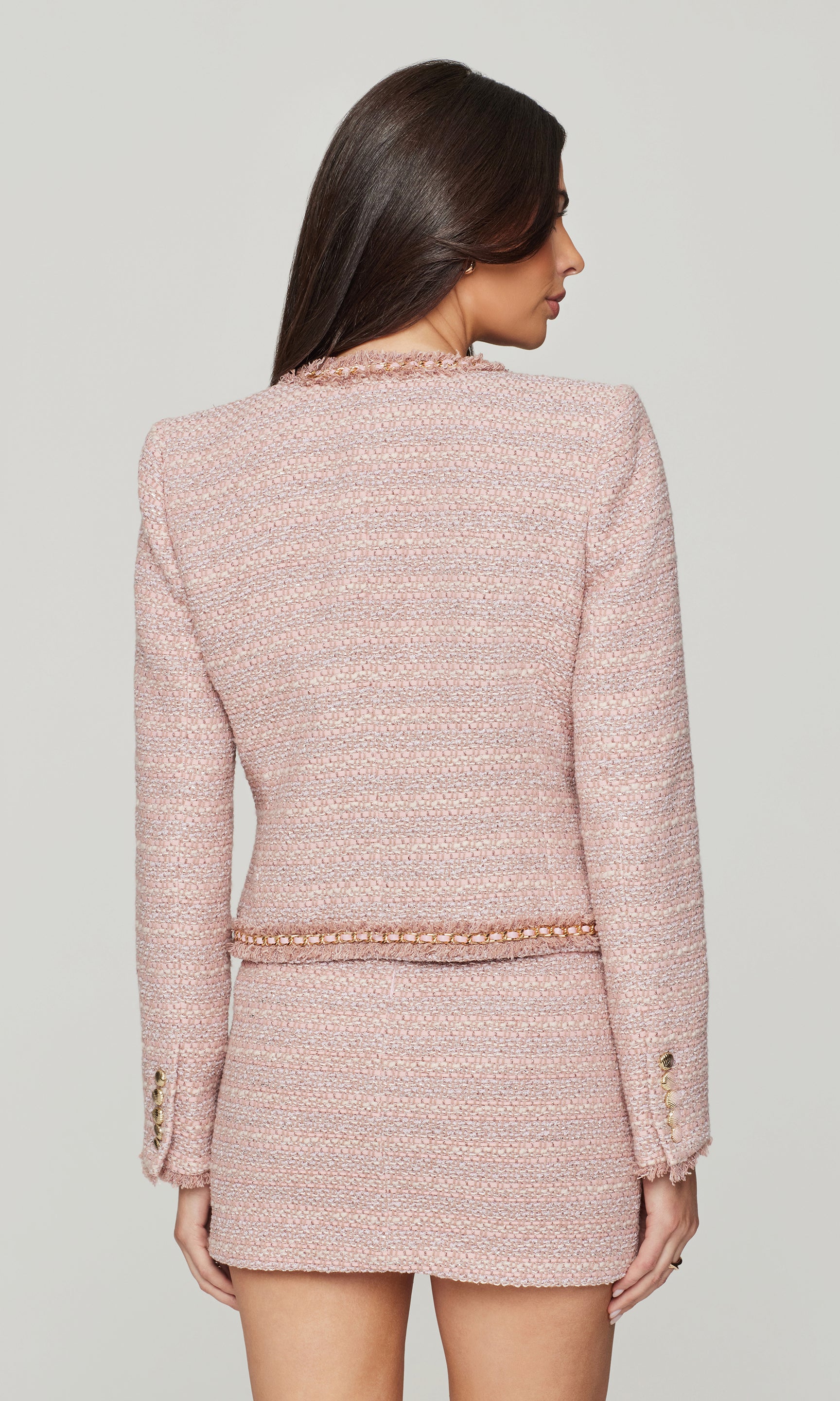 Back view of woman wearing a pink tweed suit on a plain background