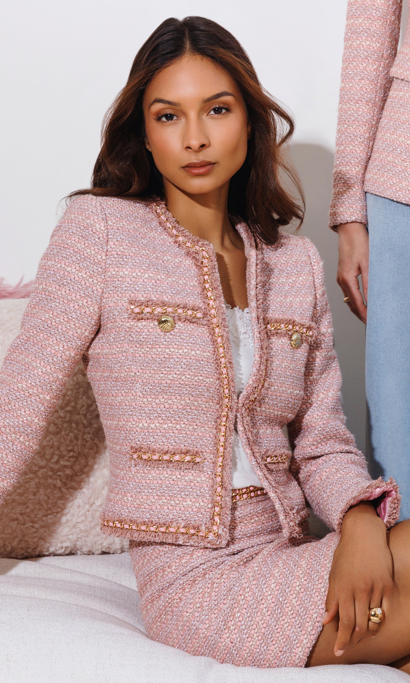 Woman wearing a pink tweed suit sitting on a white surface.