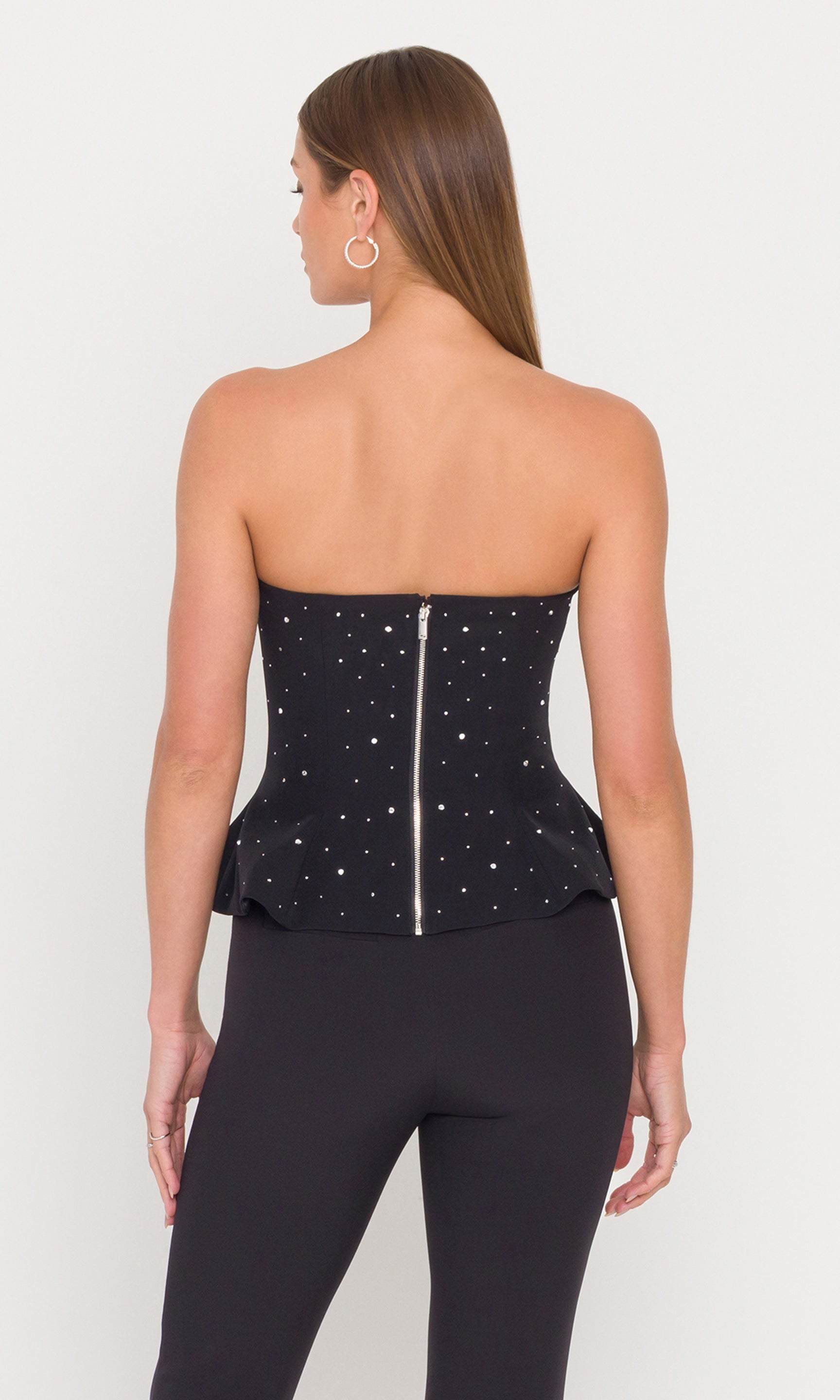 Back view of model wearing a black crystal embellished peplum bustier with black pants