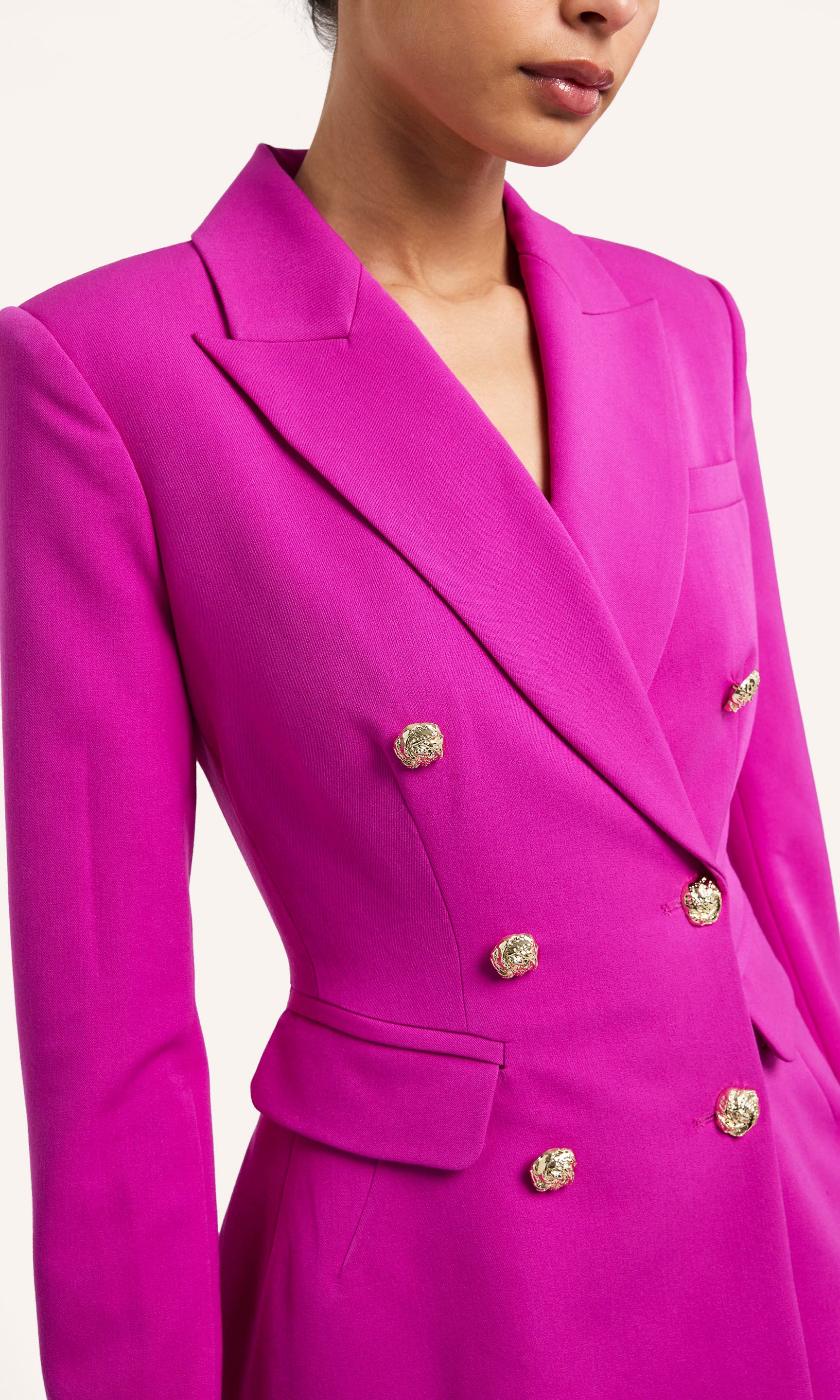 Close-up of a person wearing a bright pink blazer with gold buttons on a white background