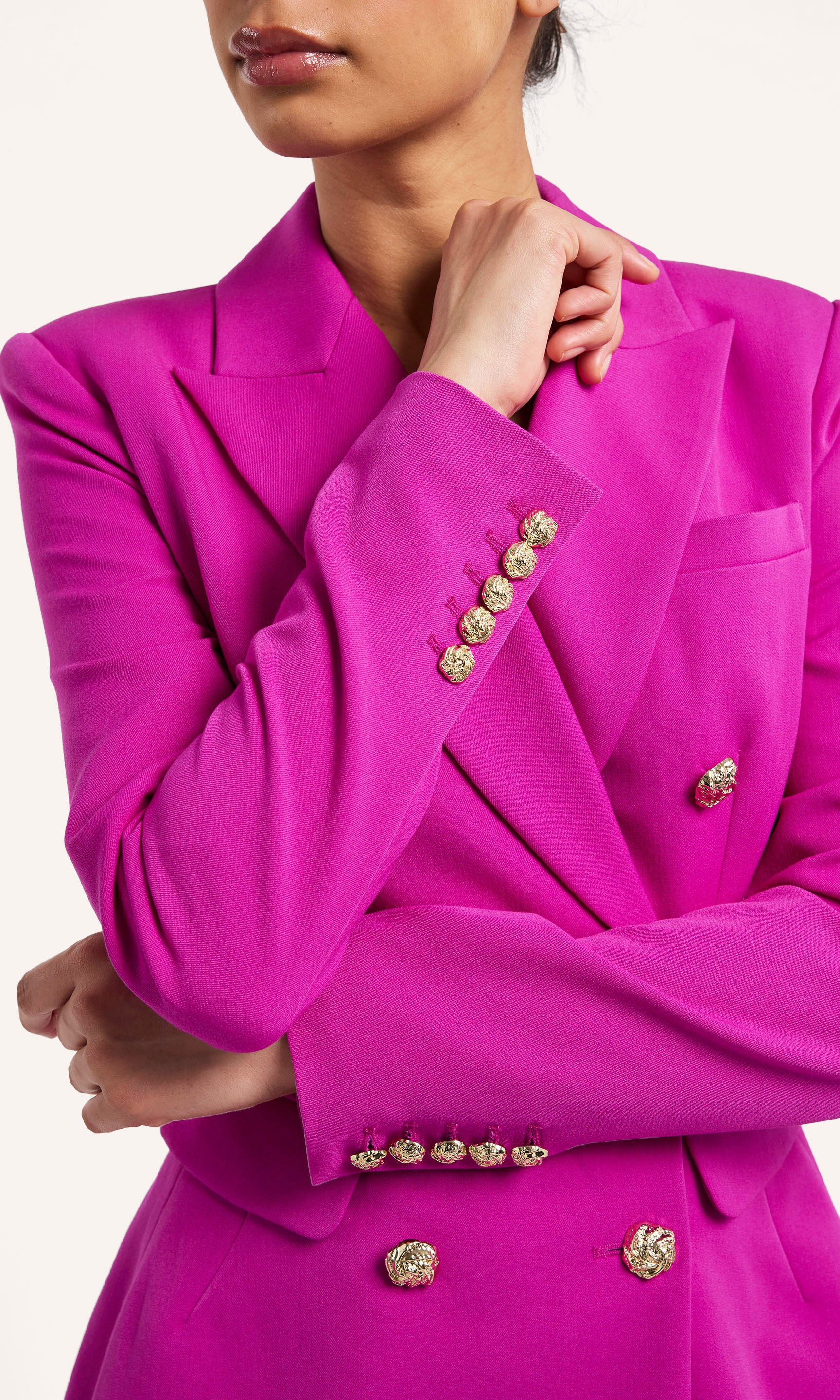 Close-up of a bright pink blazer with gold buttons on a white background