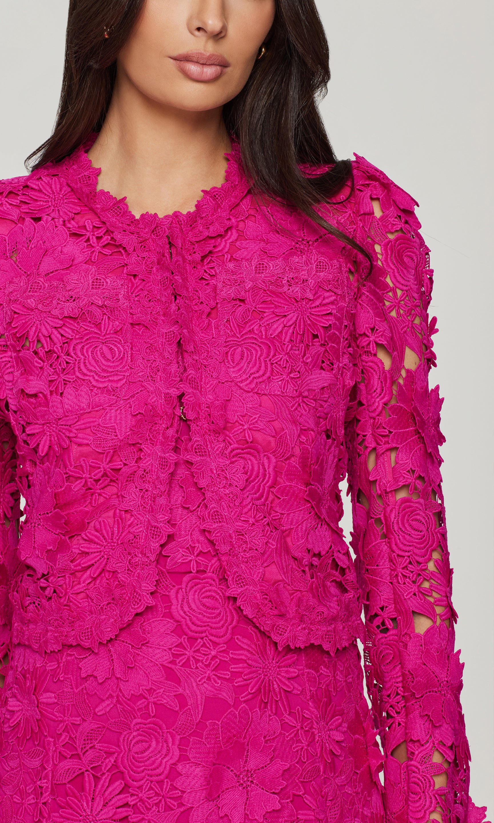 Close-up of a bright pink lace jacket over a matching dress on a plain background