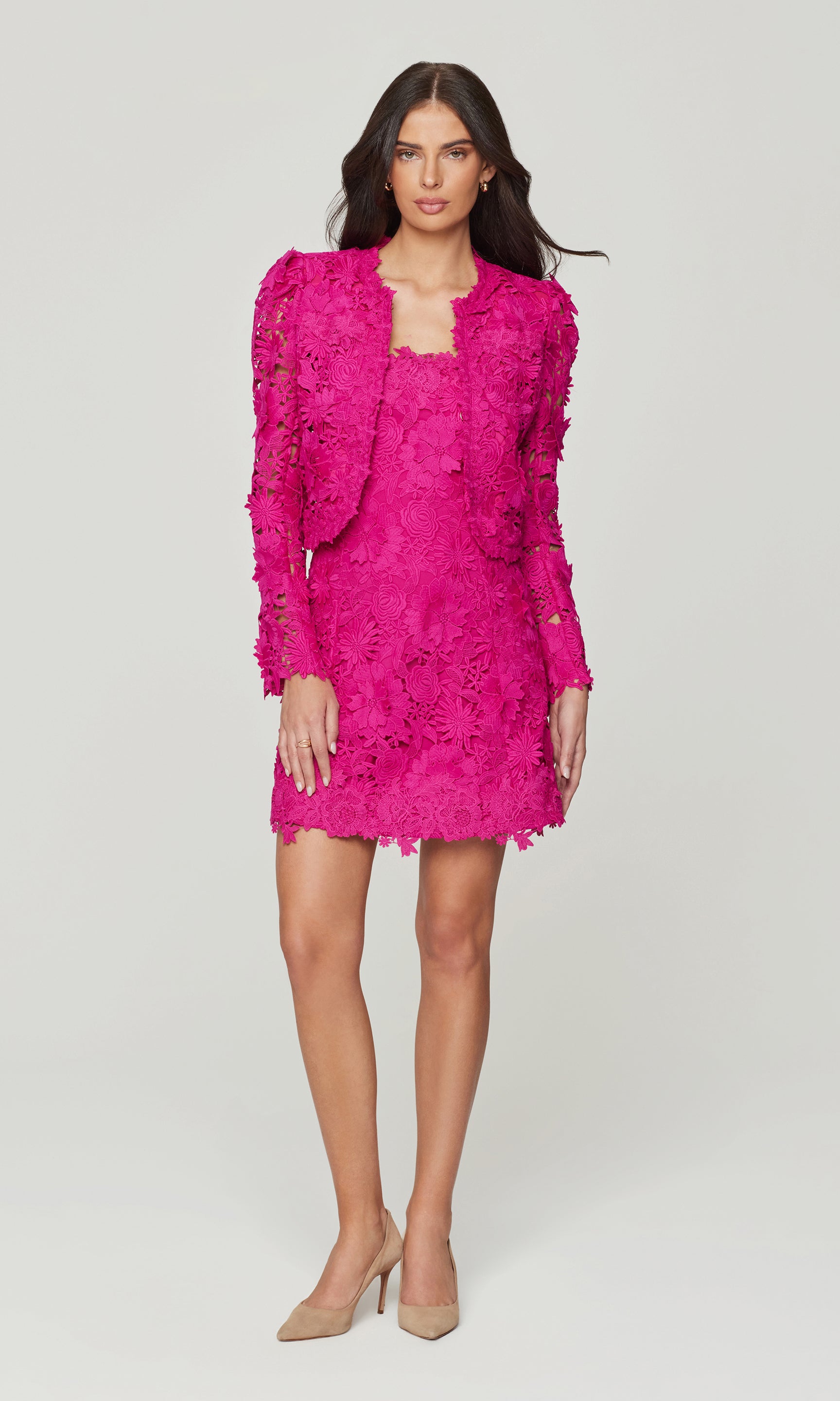Woman wearing a bright pink lace dress with matching jacket on a white background