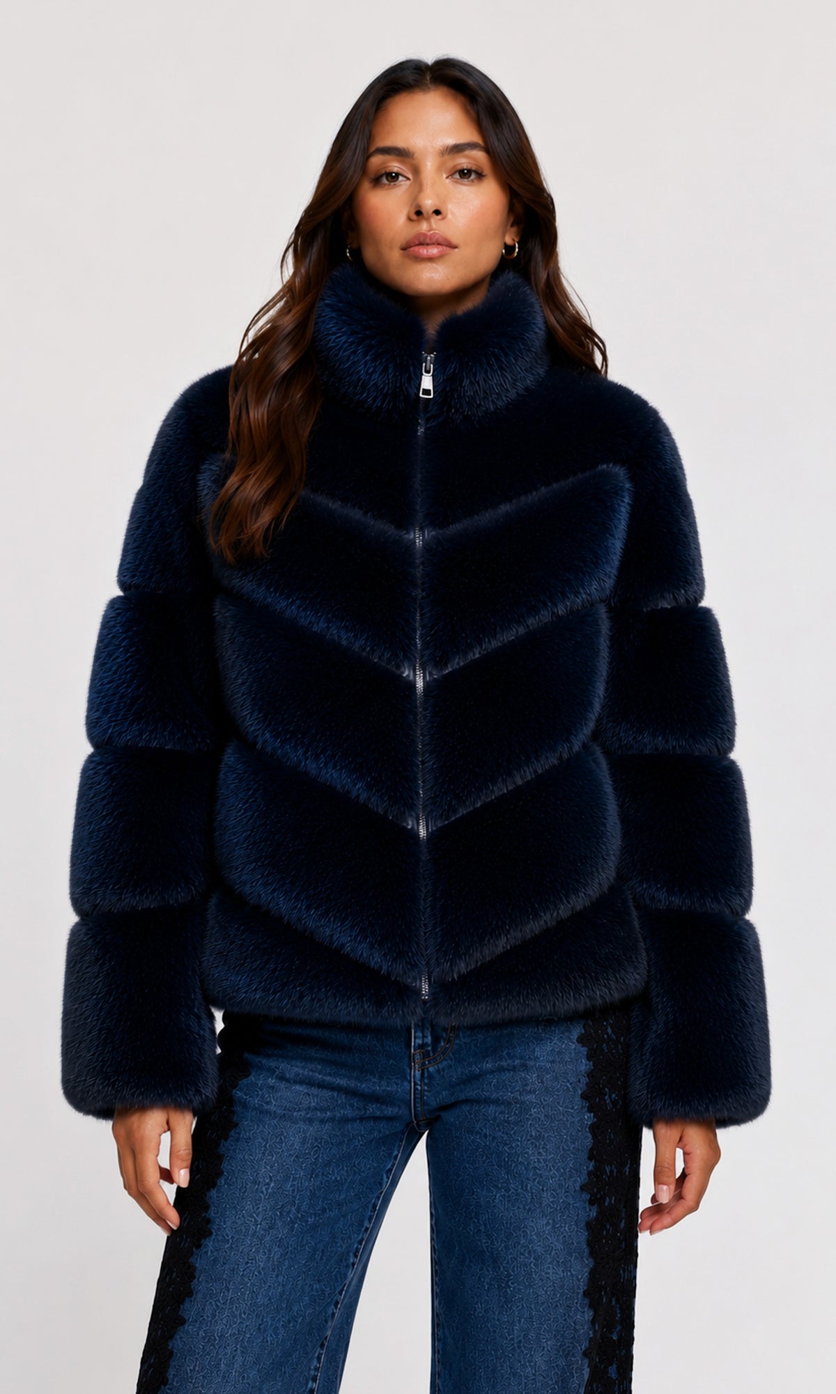 Model wearing a dark navy blue faux fur jacket with a high collar and chevron pattern, paired with blue jeans.