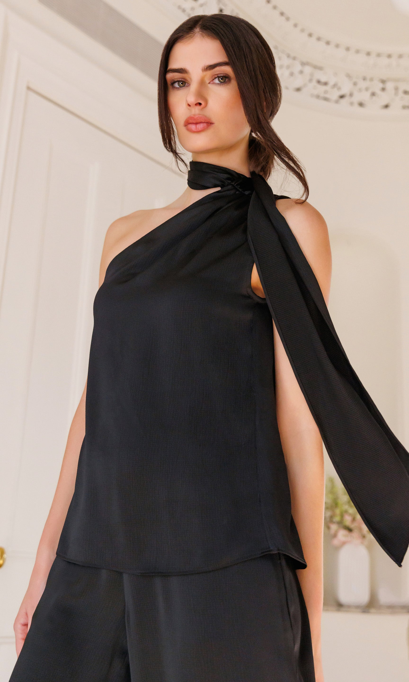 Woman wearing a black one-shoulder top with a flowing design against a neutral background