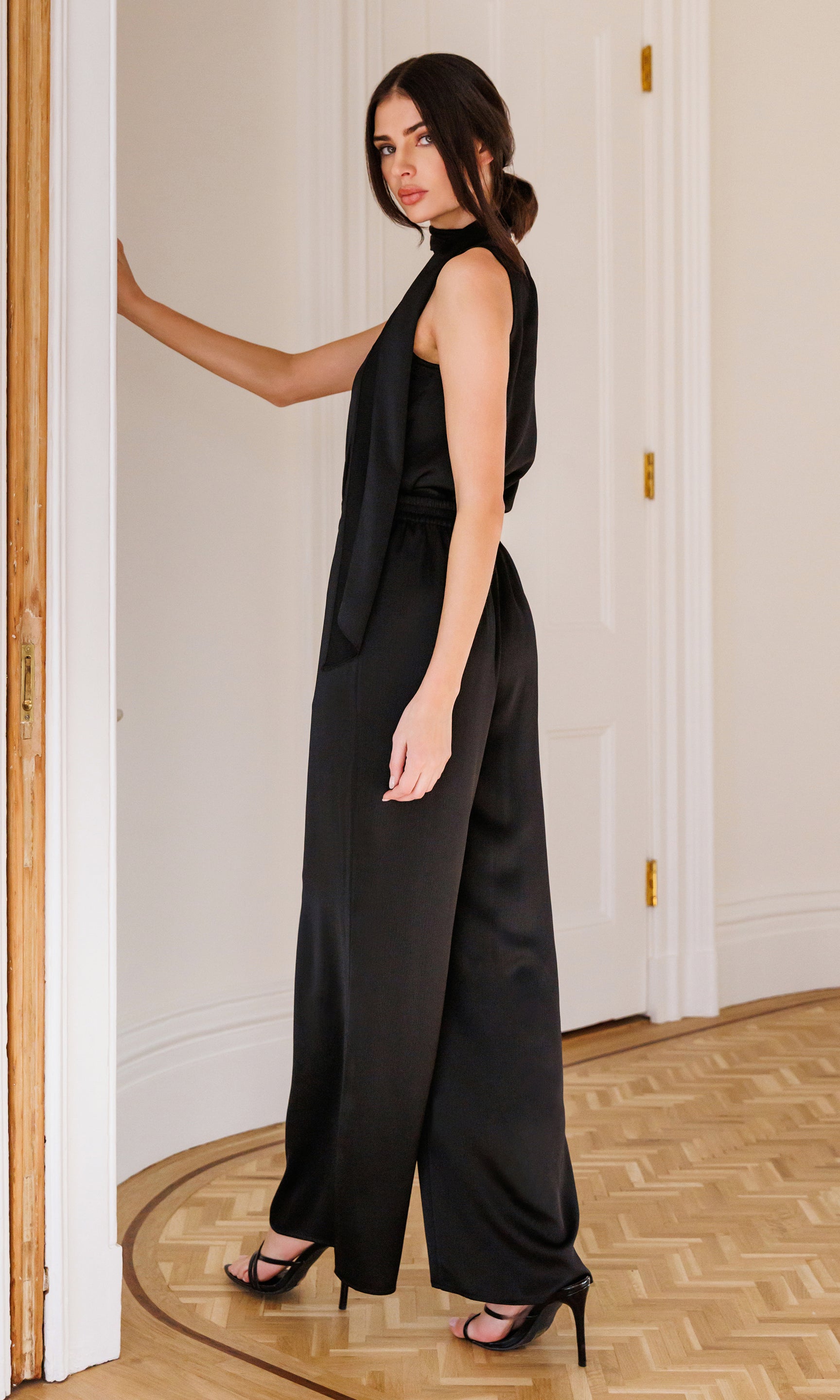 Woman wearing a black outfit standing in a room with wooden flooring and white walls.