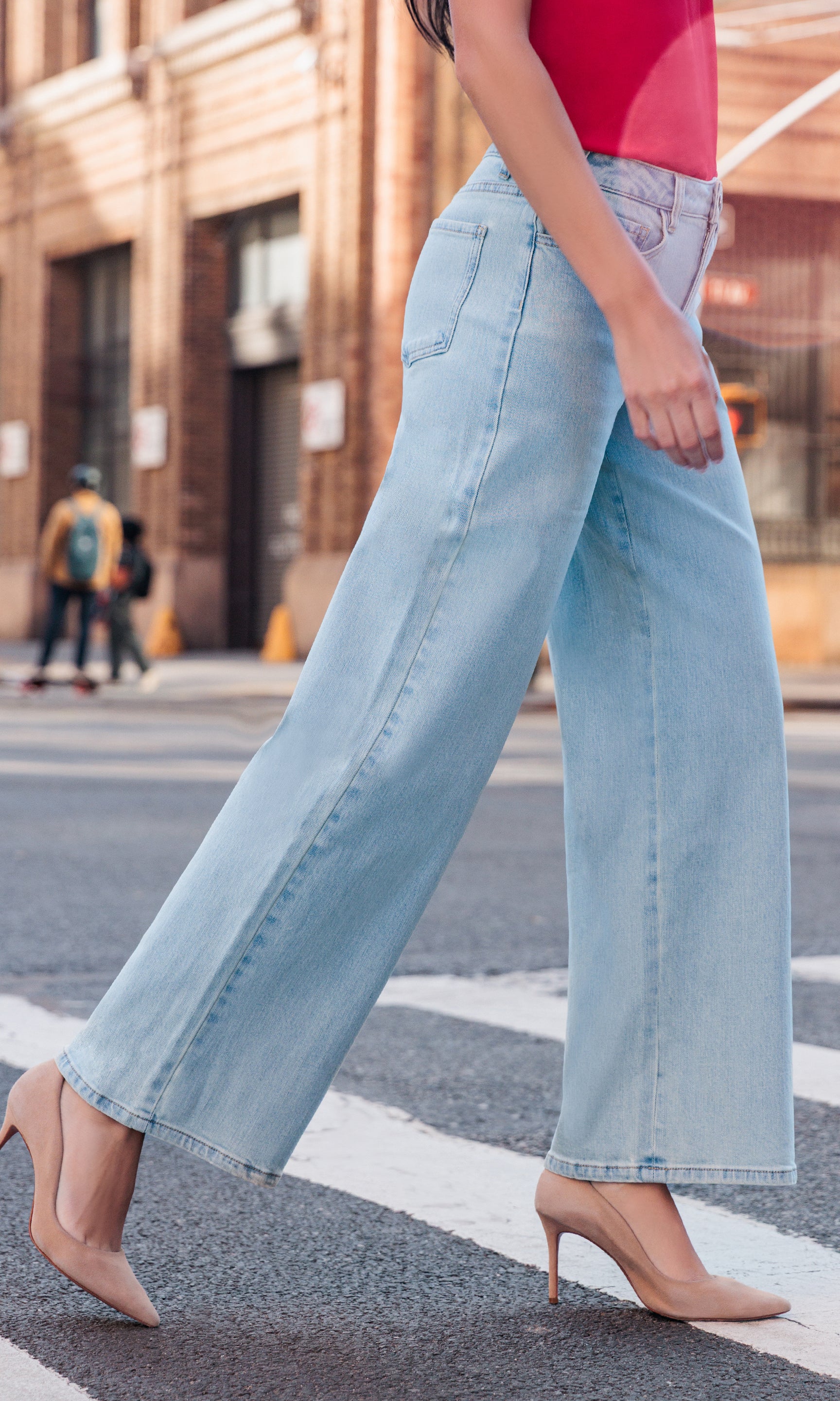 Person wearing light blue jeans and a red top on a city street.