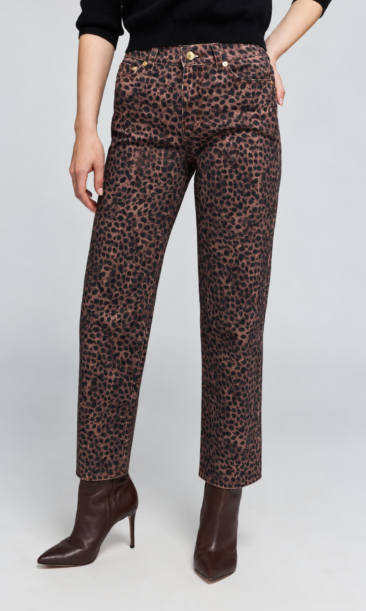 A model wearing high-waisted leopard-print trousers in brown and black, styled with a black top and dark brown pointed-toe stiletto boots against a light gray studio background.