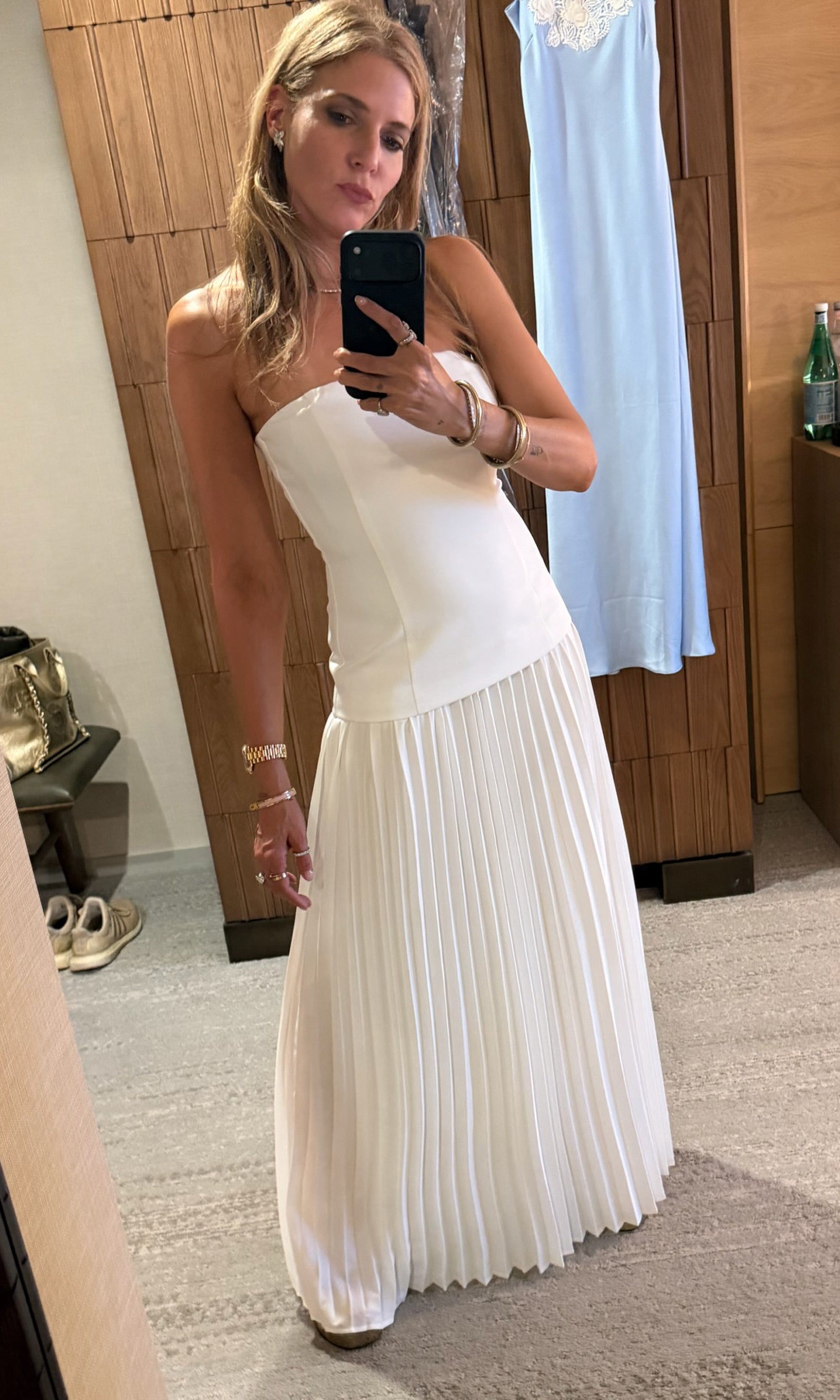 Founder Roni taking a mirror selfie wearing a white dress with a pleated bottom.