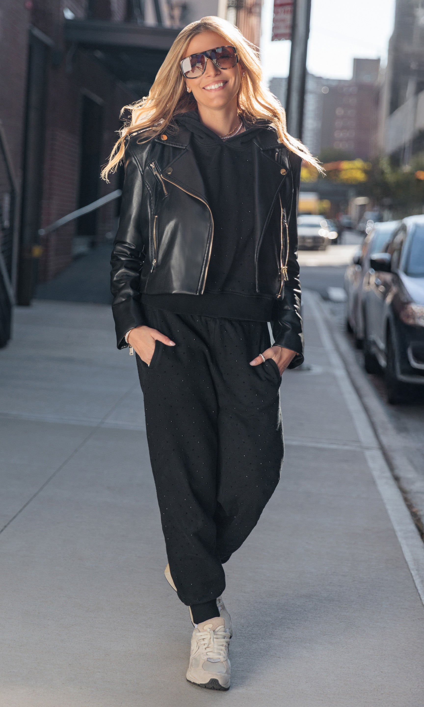 Woman in black leather jacket and jumpsuit walking on a city street.