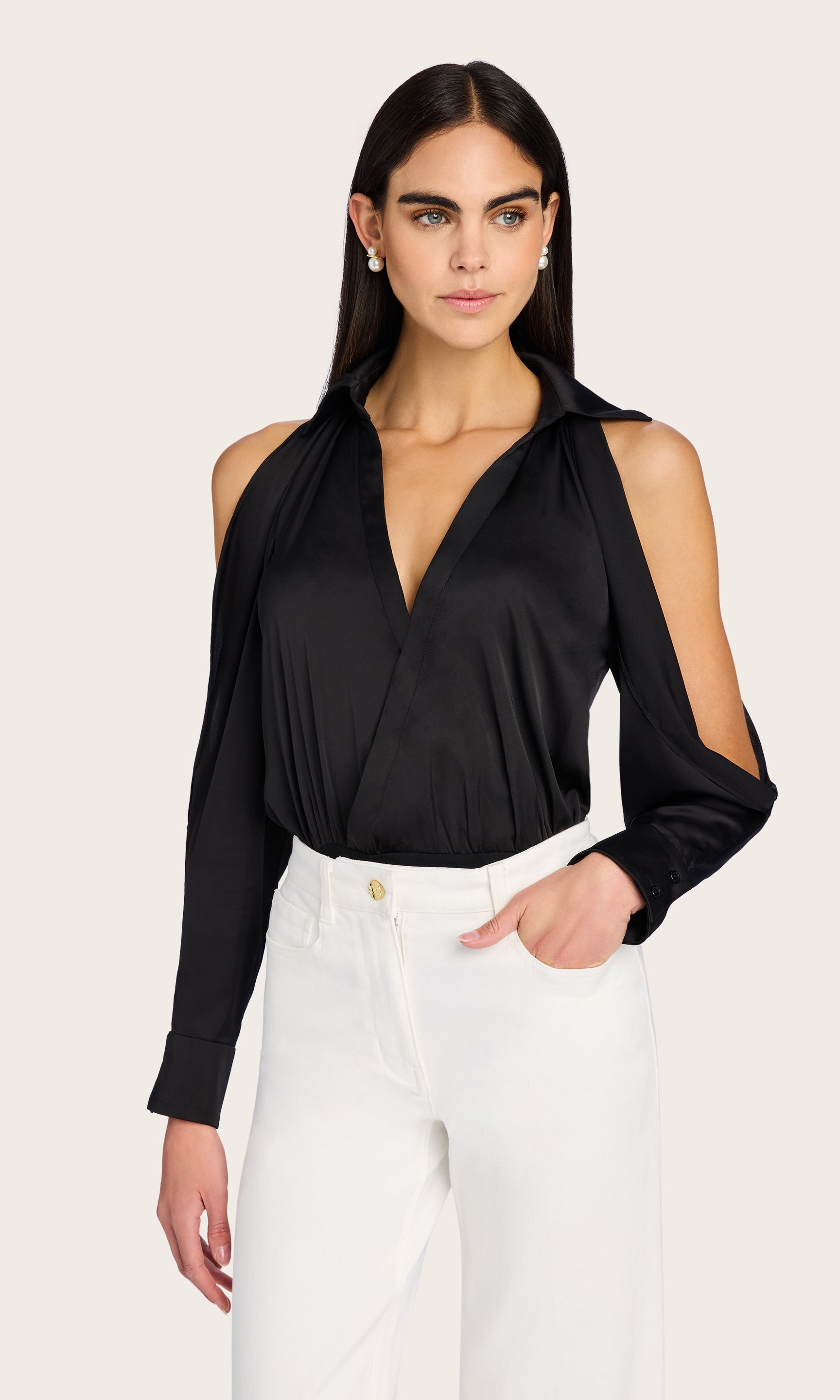 Front view of the model wearing the Dee Bodysuit styled with tailored white trousers, showcasing the deep V-neckline and cold-shoulder detail