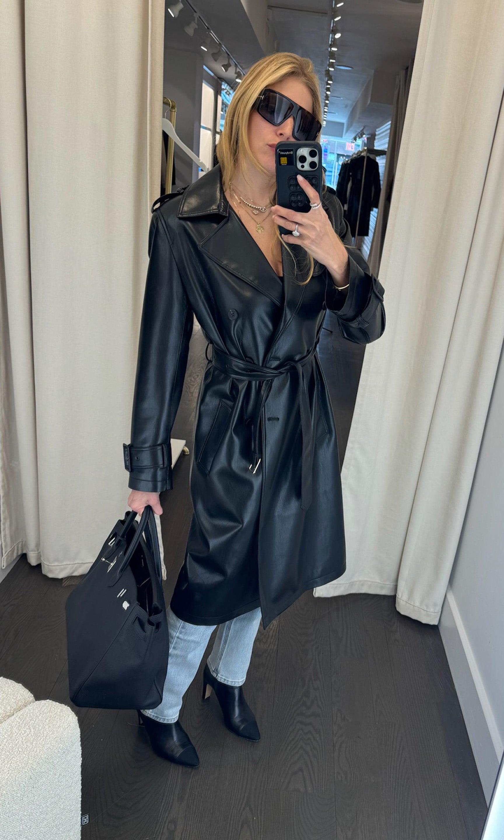 A model showcases a stylish black vegan leather trench coat, exuding elegance and modern sophistication.