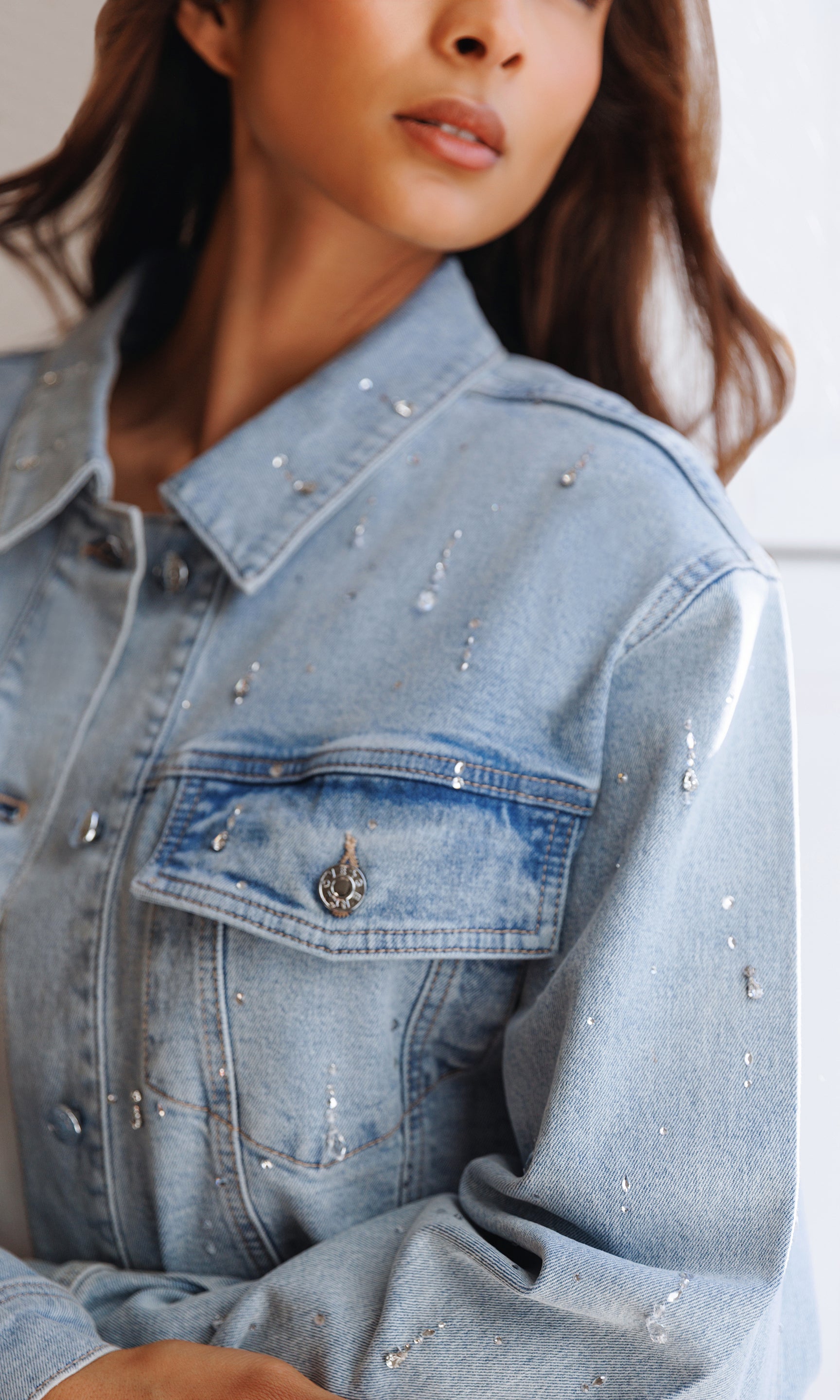 Close-up of a person wearing a light blue denim jacket with rhinestone embellishments.