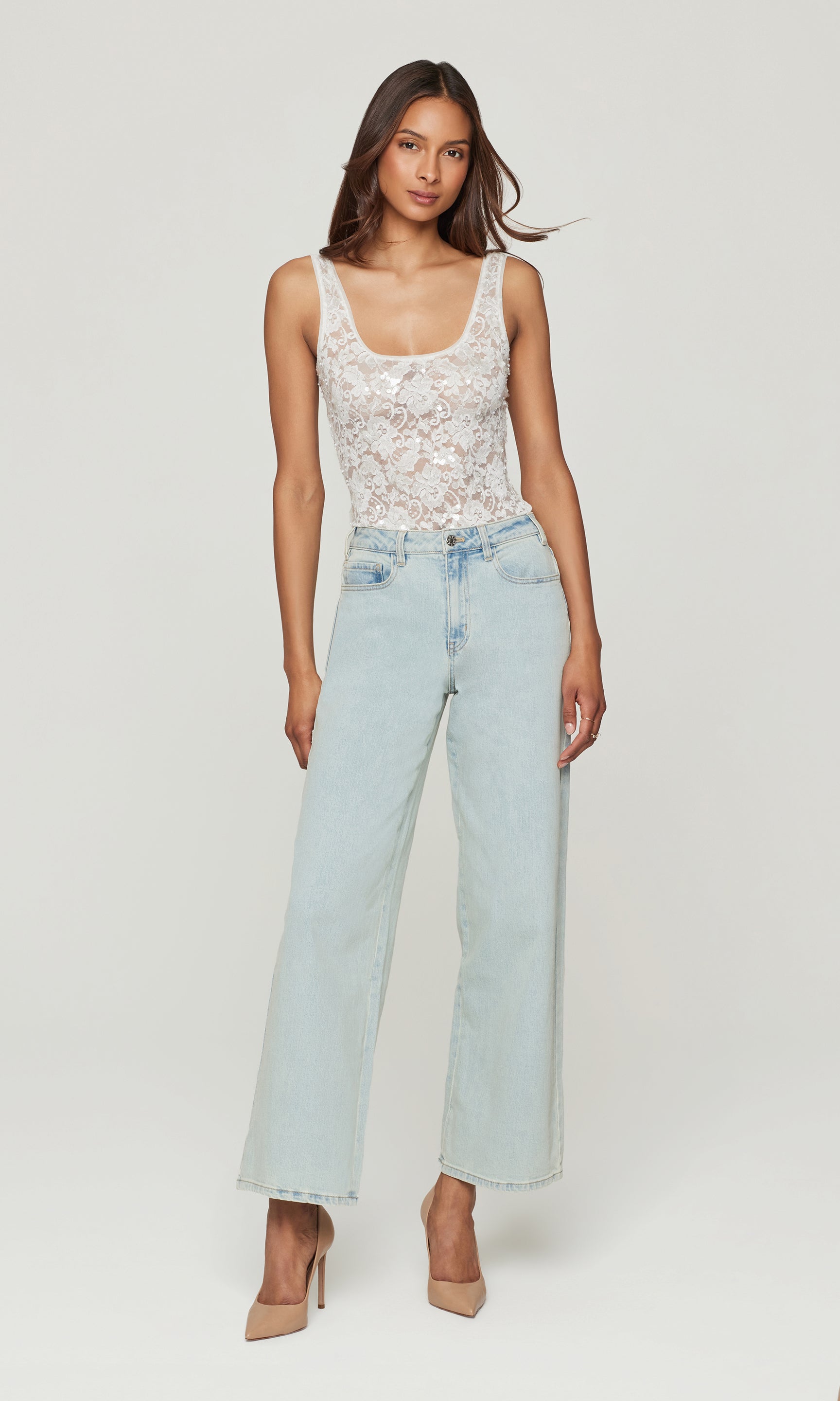 Woman wearing a white lace top and light blue jeans on a white background