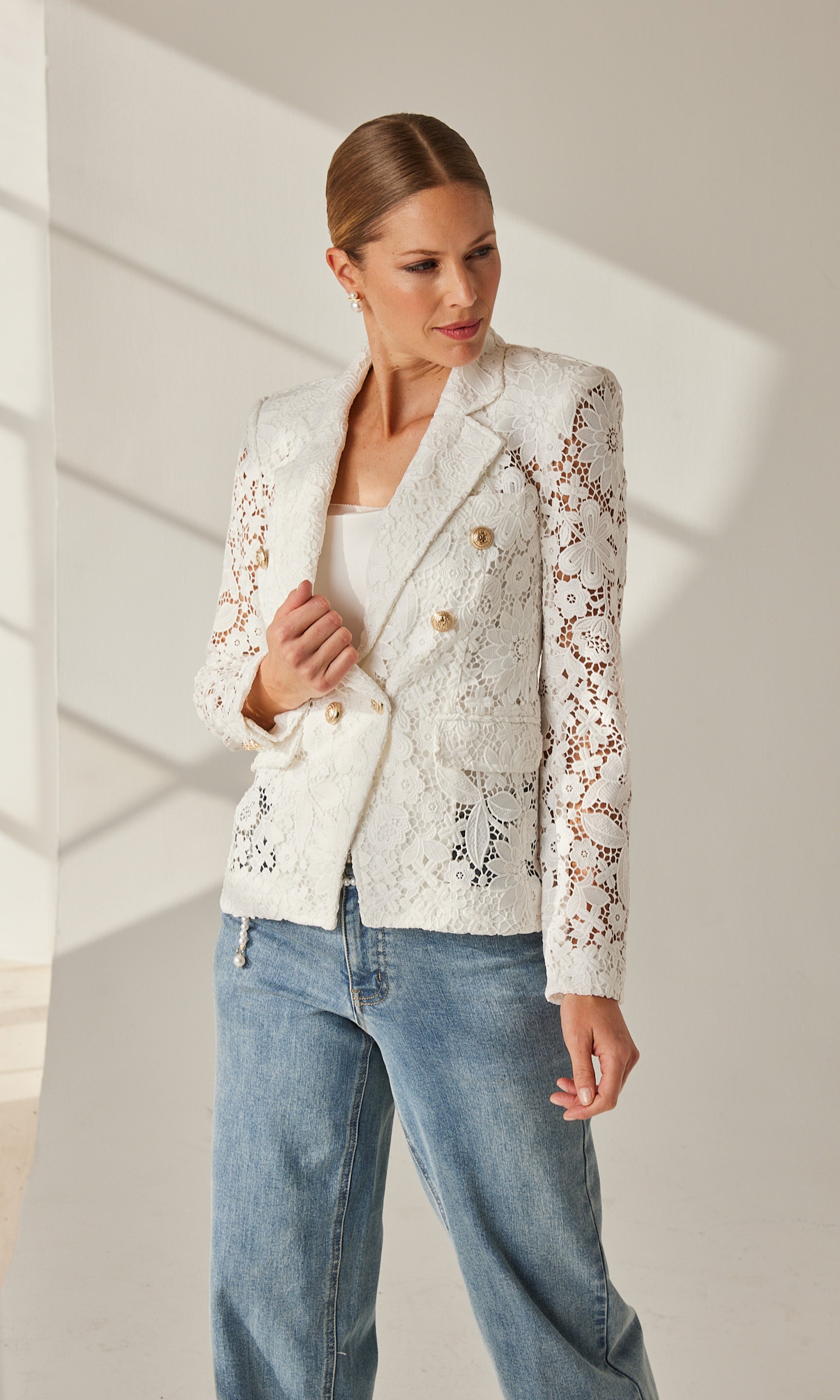 Styled indoor pose of the model wearing the white lace blazer, paired with light-wash denim jeans.