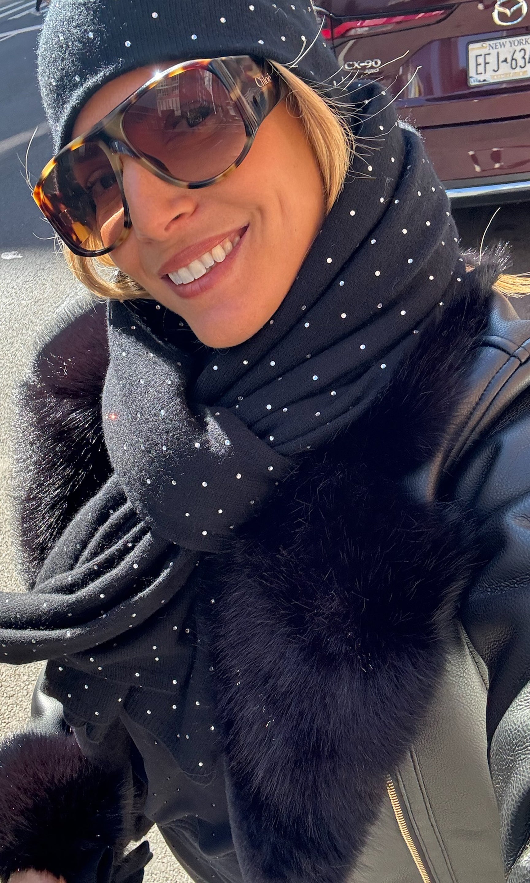 Person wearing a black polka dot scarf with a fur trim jacket in a snowy setting