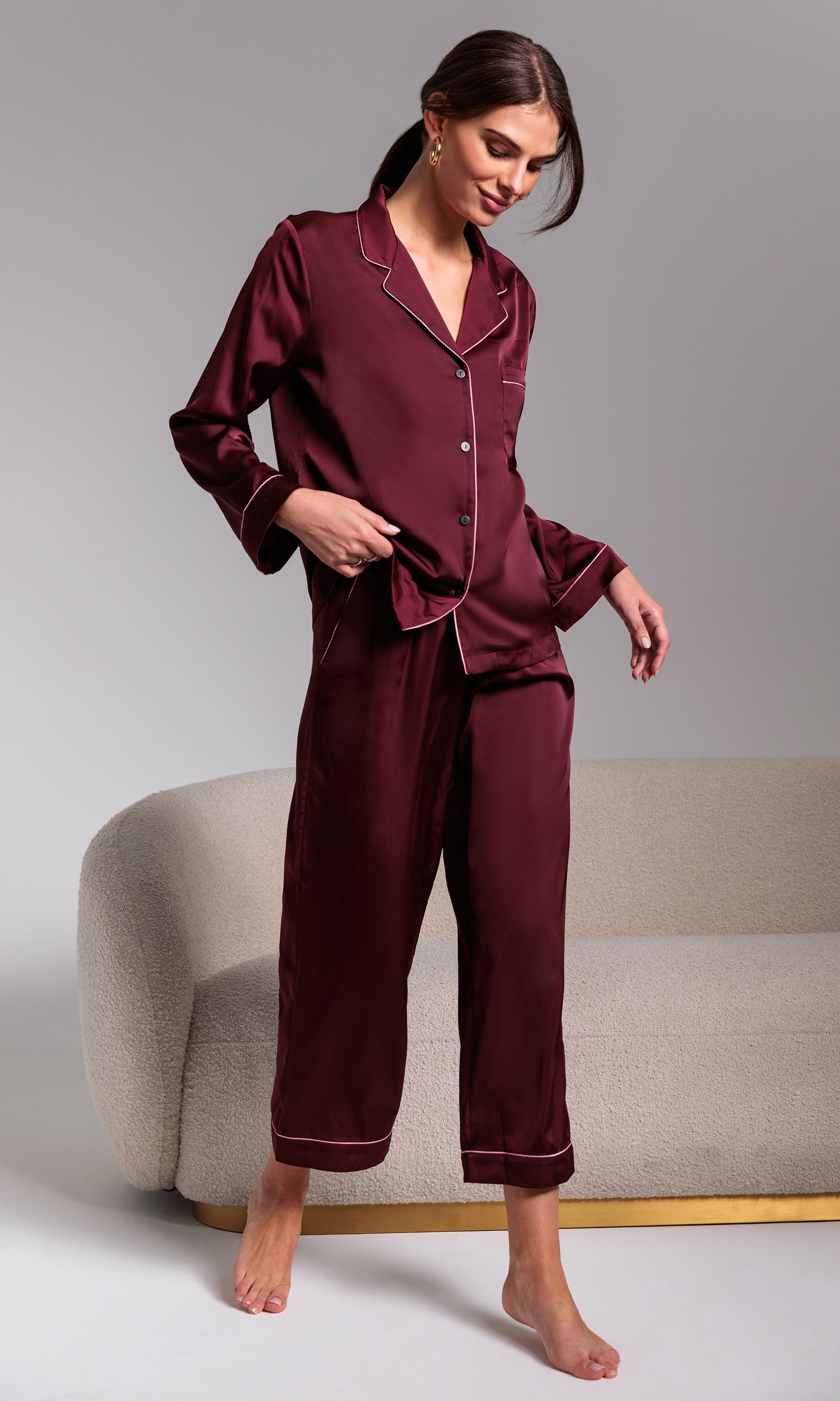 Woman wearing burgundy satin pajamas standing against a plain background