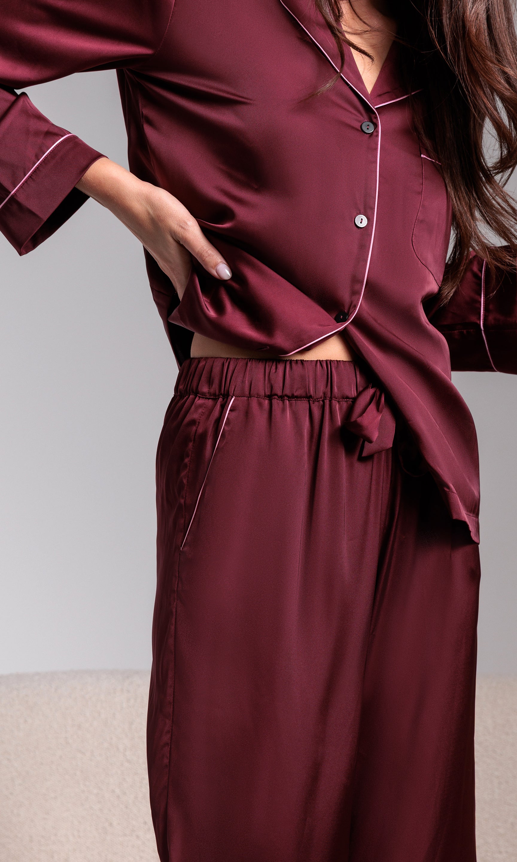 Burgundy satin pajama set worn by a person against a neutral background